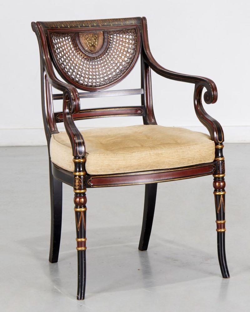 20th c., Regency style armchair, parcel ebonized with caned seat and back, lion head mount to back. The scroll arms are decorated with gold tone painted accents. There is a nice button tufted loose seat cushion. The back sabre legs are ebonized