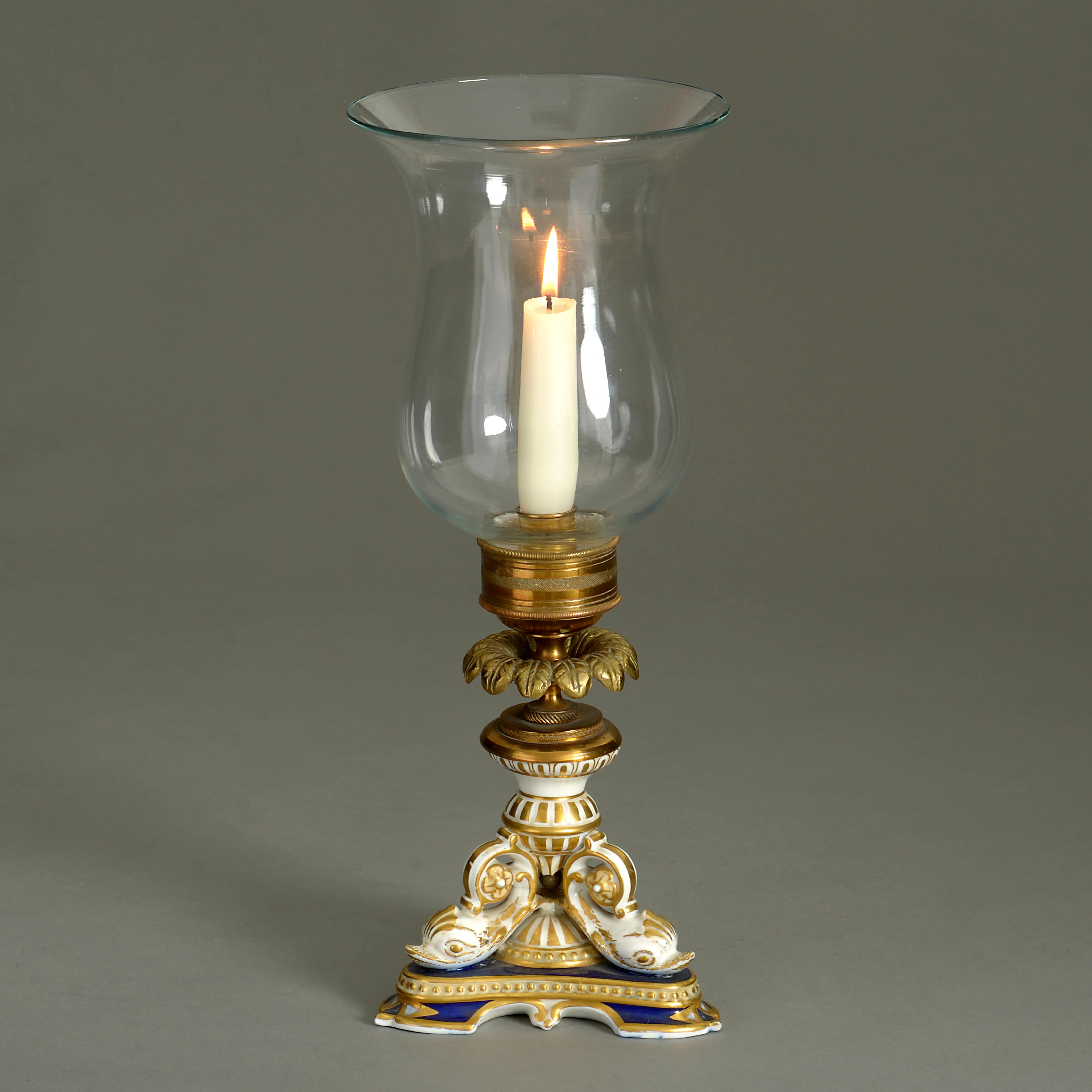A Regency style storm lantern, the glass shade supported by a porcelain plinth base with supporting dolphins in blue, white and gold glazes. With red glazed factory marks to the underside.