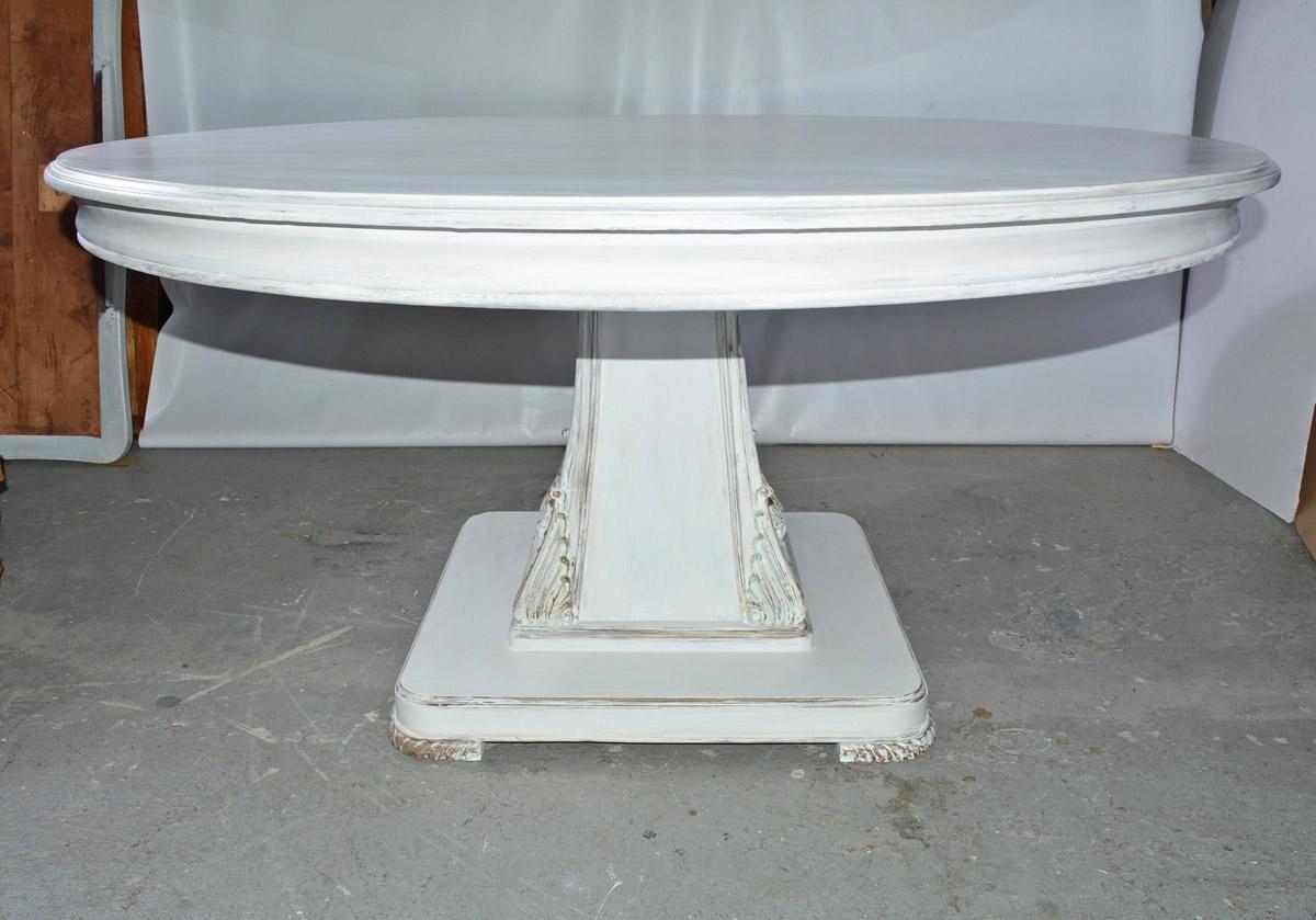 The round dining table has a square empire style pedestal base embellished at the corners with stylized acanthus leaves and rope-like feet. The painted mat finish is brushed white slightly distressed. Seats up to eight people. Table can be used as
