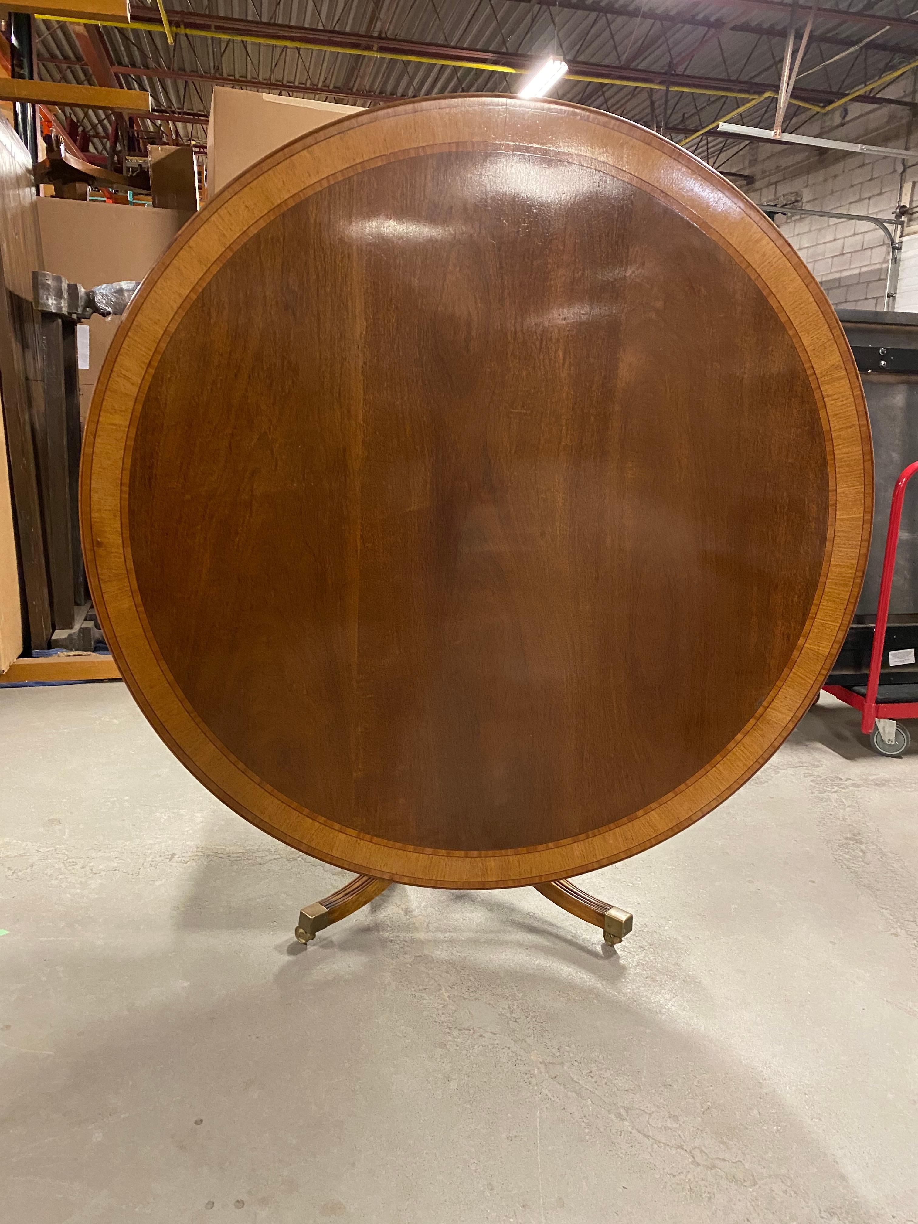 A beautiful Regency style mahogany tilt-top dining or centre table. The Classic banded top with satinwood and walnut sits on a mahogany pedestal with the splayed feet ending and supported on the box style brass toe caps and brass casters. This table