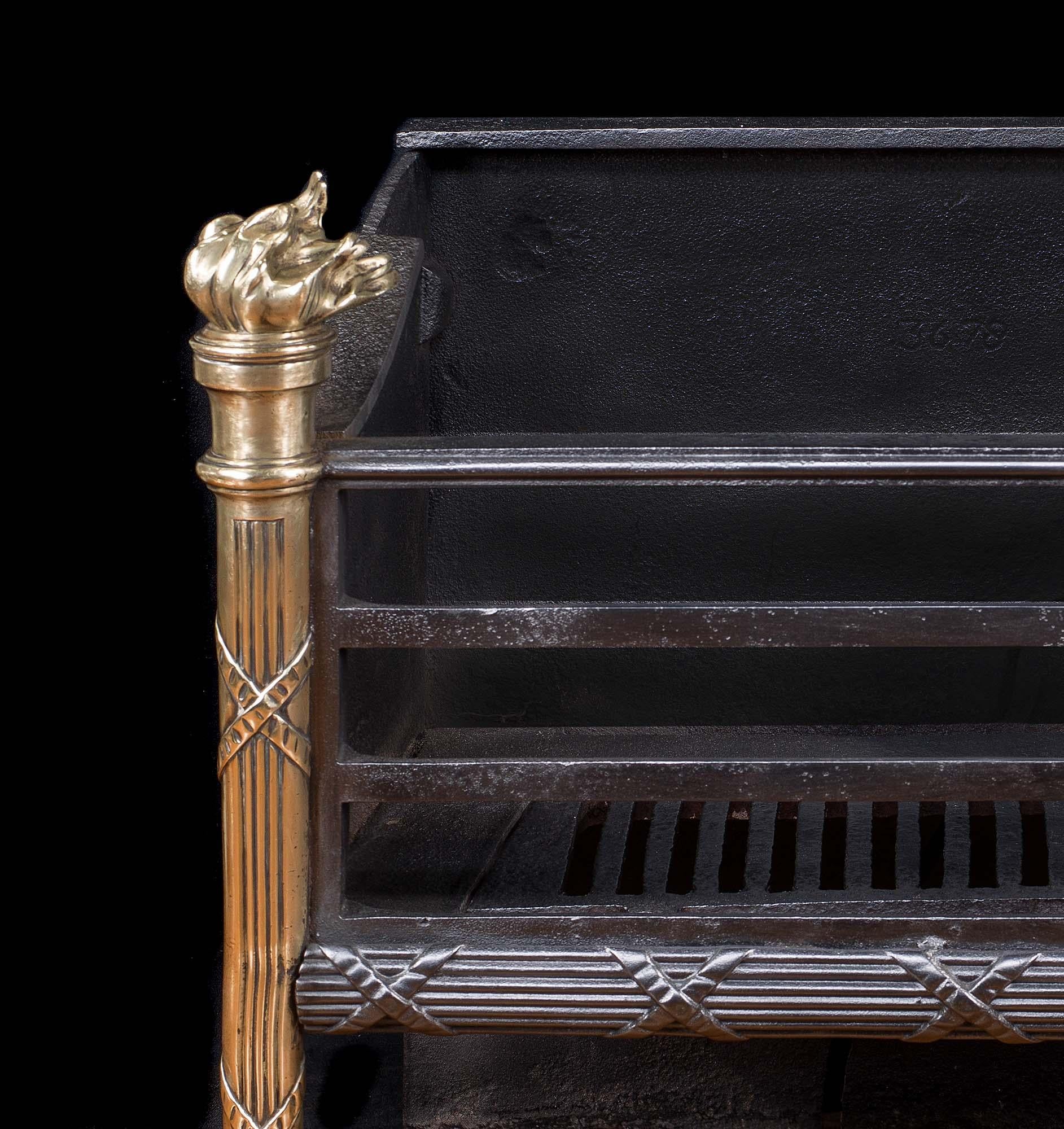 A small and elegant Regency style brass and cast iron three bar fire grate.The brass, flambeau topped, tapering, ribboned torchere legs are linked by a cast iron cross tied bar. Charming and understated. English, circa 1900.
       