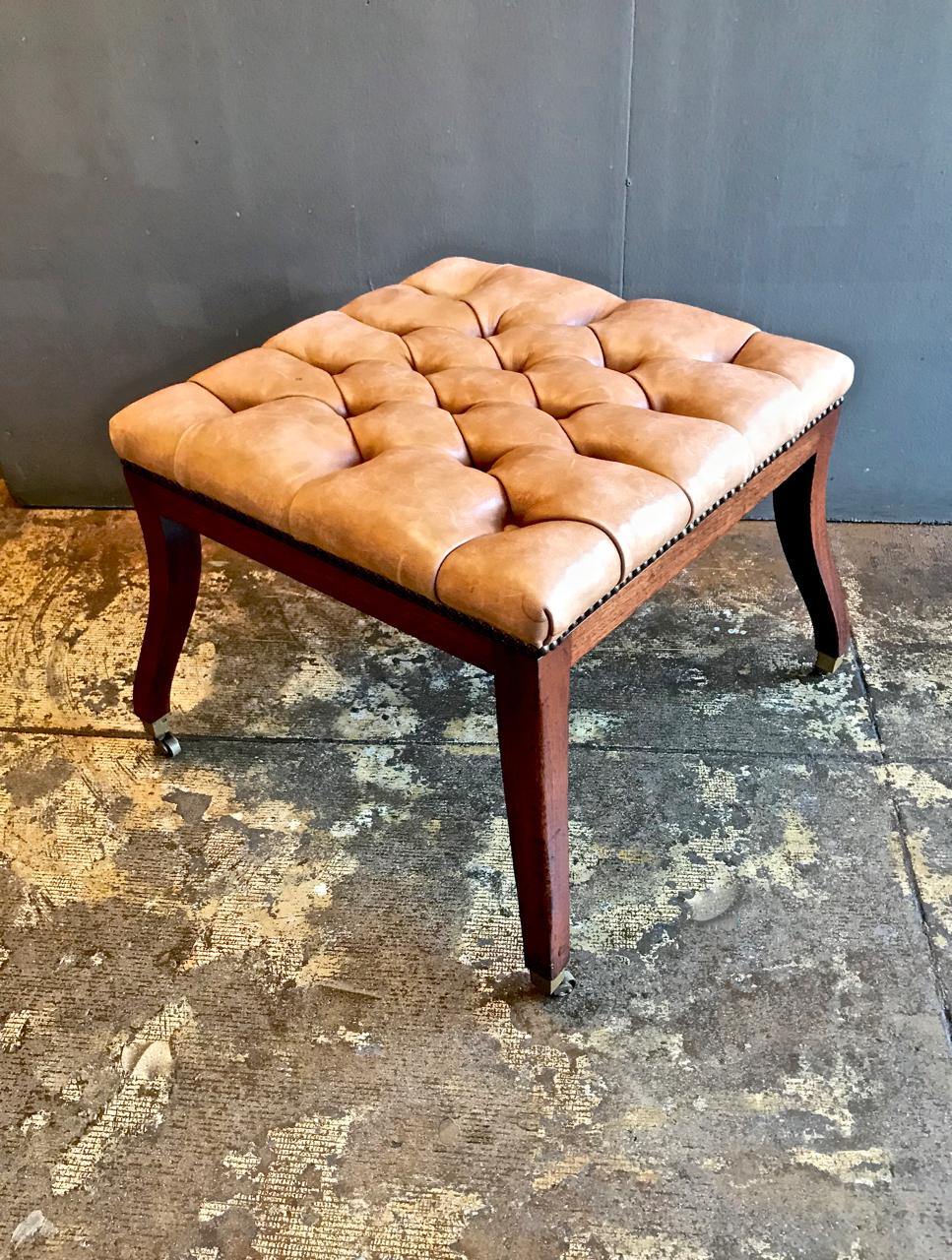 This is an unusual Regency-style tufted leather bench. The elegant legs are out-swept ending in small casters in a high early 19th century form. The tufted leather has great natural patina.