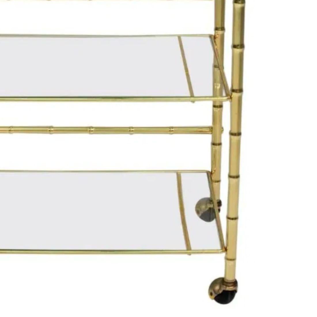 Il carrello da bar in ottone e bambù a più livelli in stile Regency presenta un'elegante struttura in ottone con un design in finto bambù, che riflette l'estetica sofisticata dell'epoca Regency. I suoi ripiani in vetro a tre livelli offrono ampio