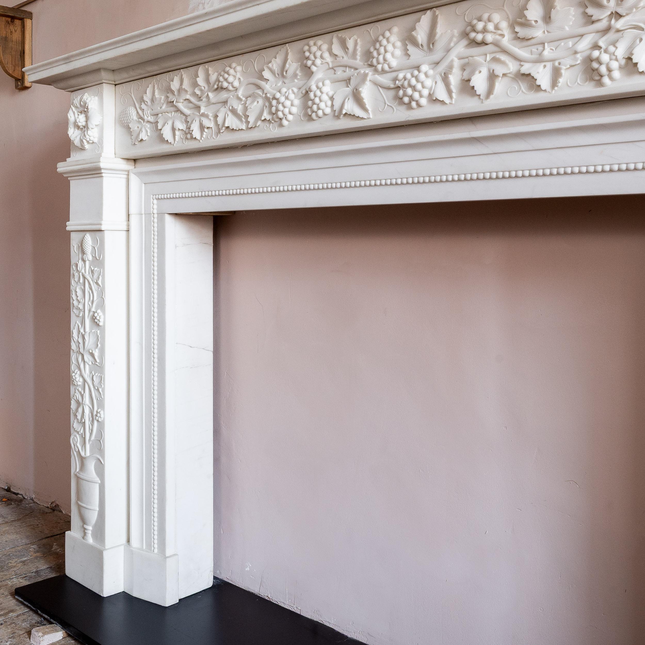 Regency style white marble fireplace, modern,with stepped rectangular shelf above a frieze adorned with trails of vine leaves and grapes wrapped round a Thyrsus, all emblematic of the Roman God Bacchus, the jamb panels carved in a similar manner