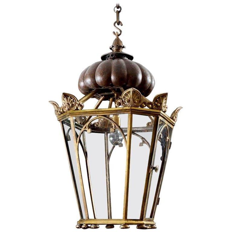 A Regency style hanging lantern with faceted, Gothic panels topped with hipped, anthemion decorated, classical antefixes; the hole upheld by a circular, rounded and ribbed clasp, capped with a finial.
 