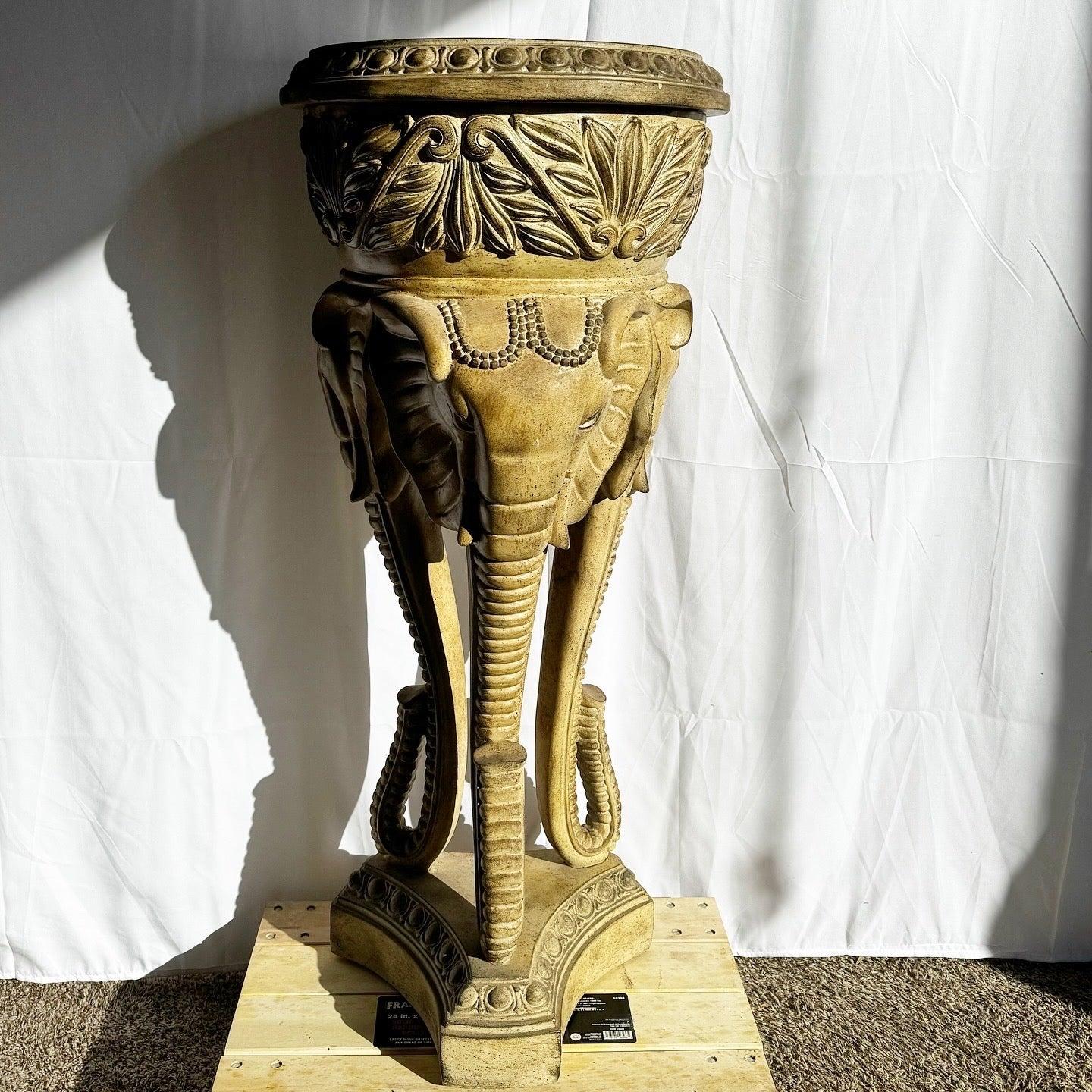 Regency Elephant Plant Stand featuring intricately detailed elephant heads and ornate floral carvings, perfect for adding exotic charm to your decor.
 
 Has a crack at the base of one of the tusks as shown and is a little loose. Also there are