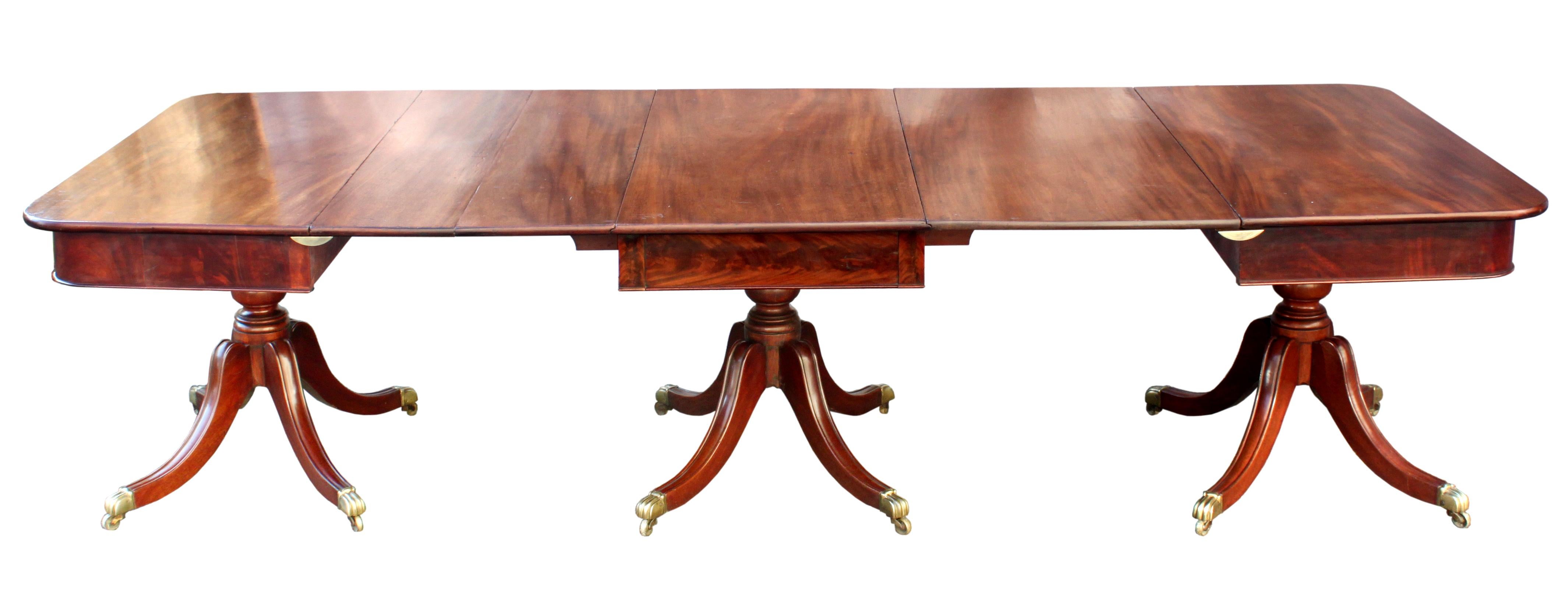 An attractive Regency dining table in figured mahogany, the veneered frieze above three elegant 4 splay bases: handsome turned pillars and sabre legs with carved moulded tops and the original brass sabot castors of a similar moulded design. Folding