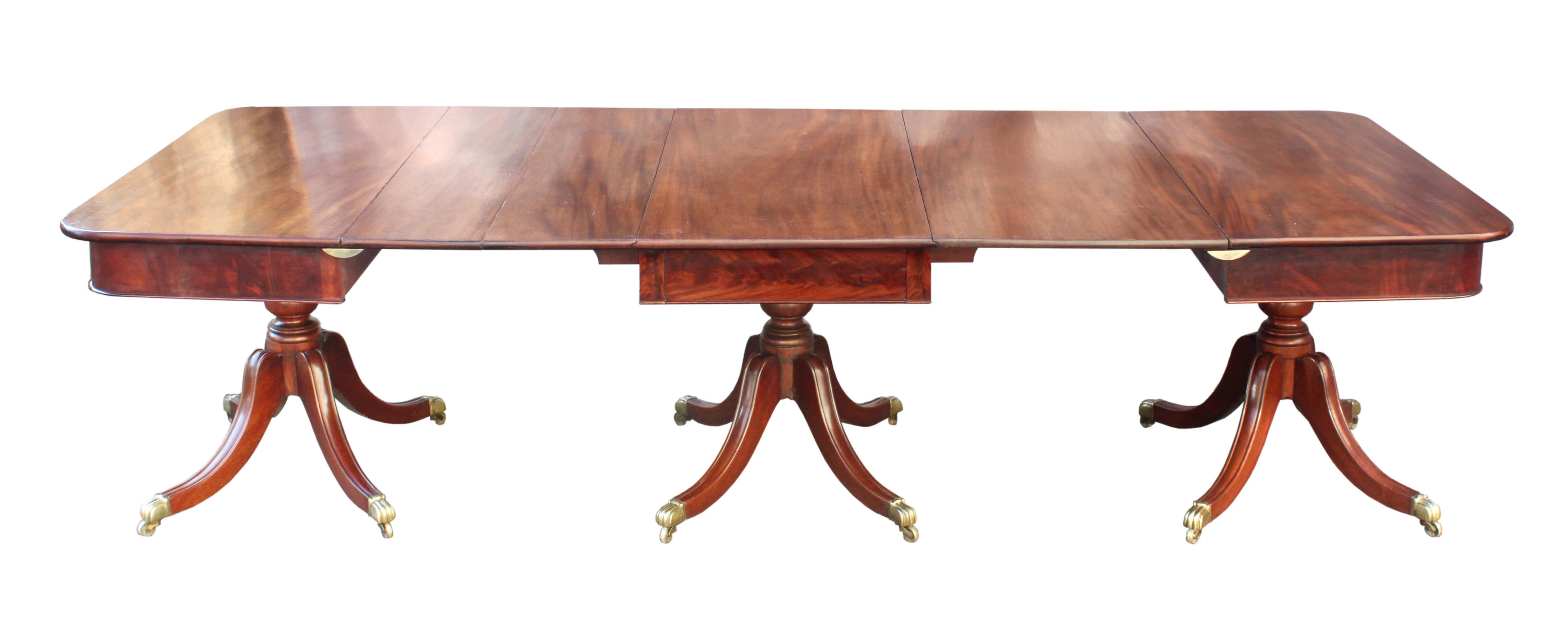 An attractive Regency dining table in figured mahogany, the veneered frieze above three elegant 4 splay bases: handsome turned pillars and sabre legs with carved moulded tops and the original brass sabot castors of a similar moulded design. Folding