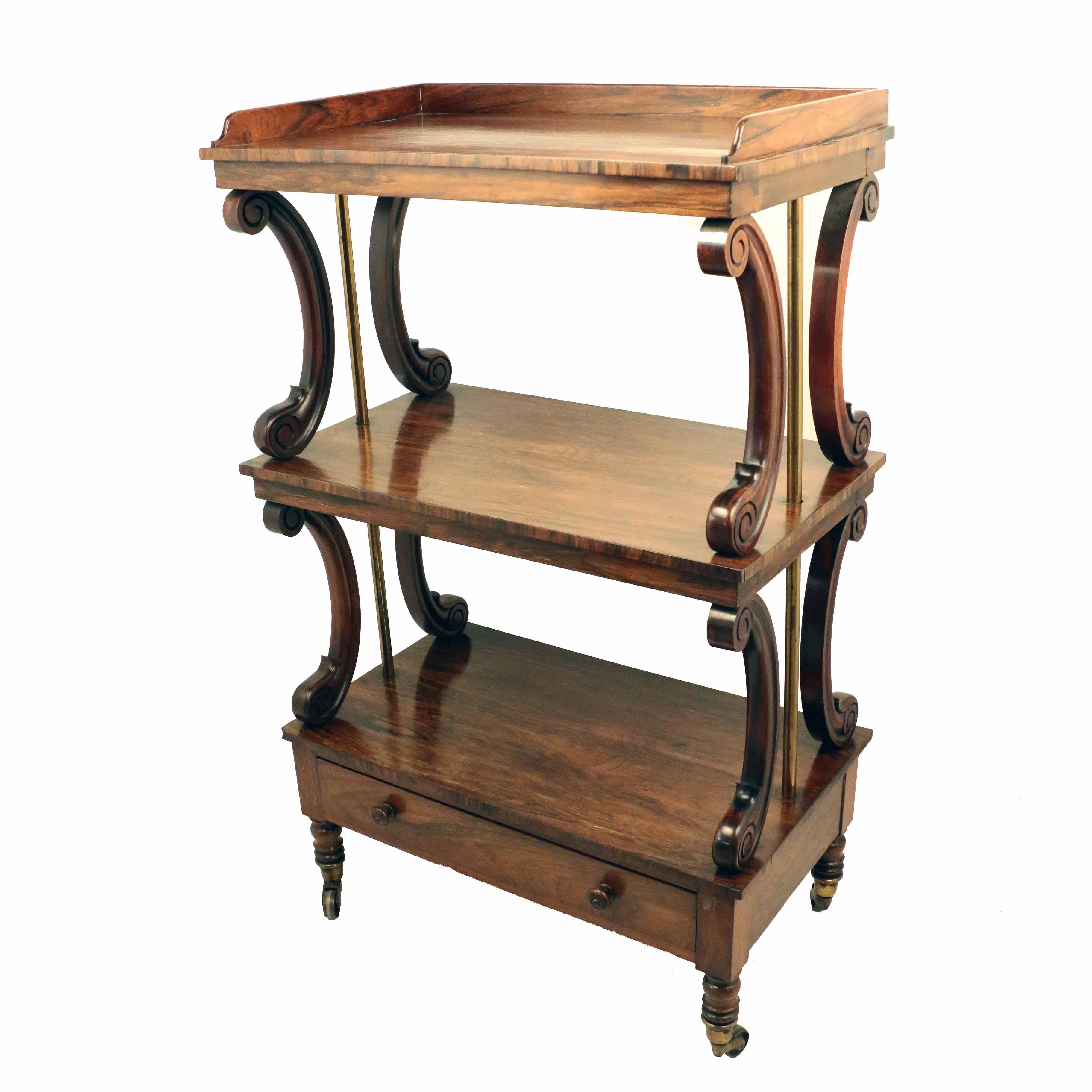 Regency three-tier strongly figured mahogany whatnot, the top shelf with three quarter gallery,  flanked by scrolled uprights to lower shelves, with single drawer, raised on turned legs with cappings and casters.
This is a classic Regency whatnot,