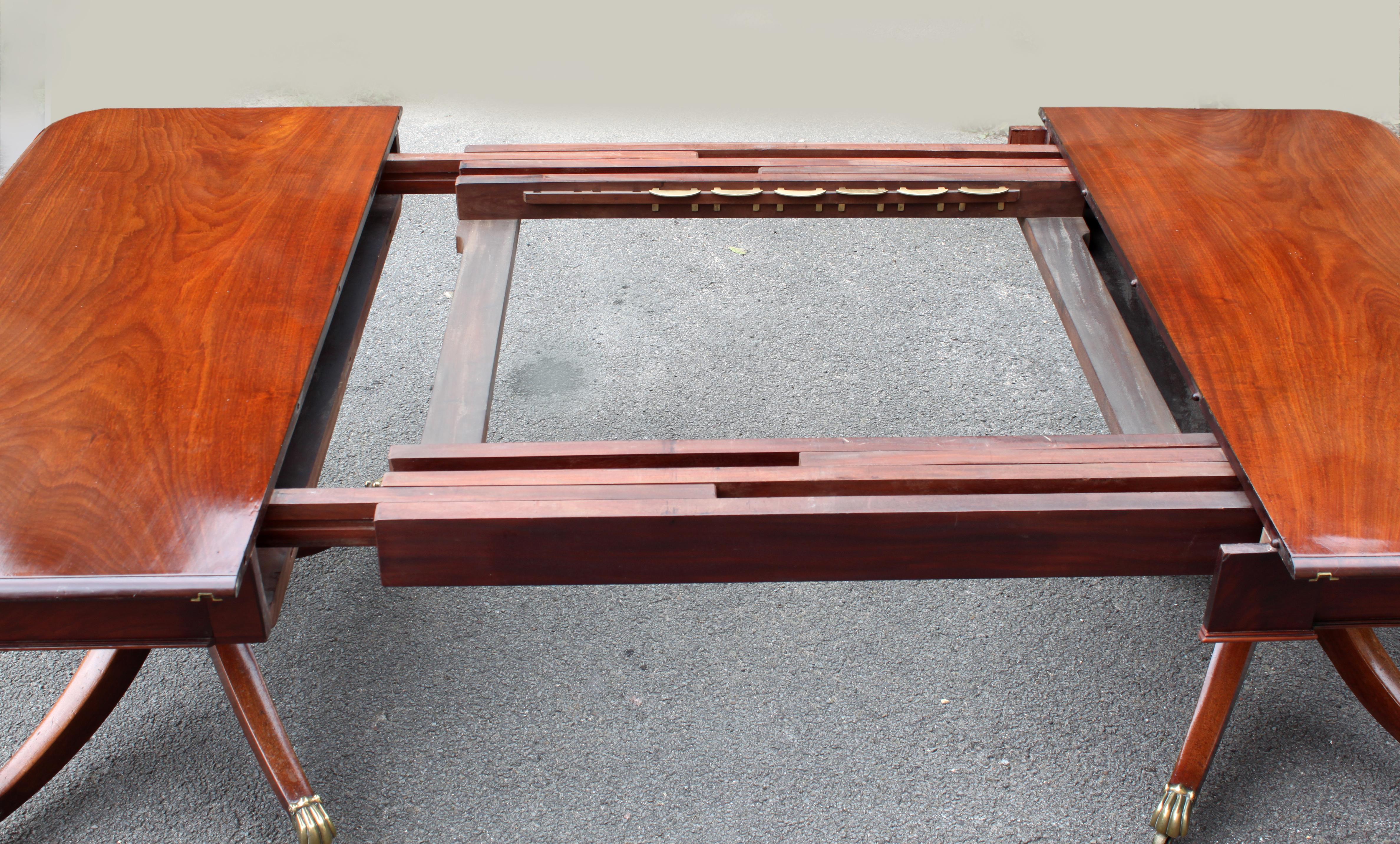 A fine Regency dining table with rare telescopic extending action; figured mahogany; elegant twin 4-splay pedestals with handsome brass casters; attractive frieze and tablet.