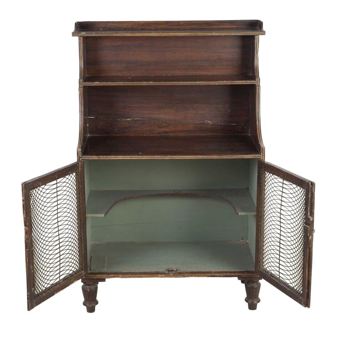 A Regency faux rosewood decorated waterfall bookcase with intricate wire trellis work on the panelled doors. English, circa 1820.

During the first 30 years of the 19th Century, the use of low cabinets with display shelves became very popular
