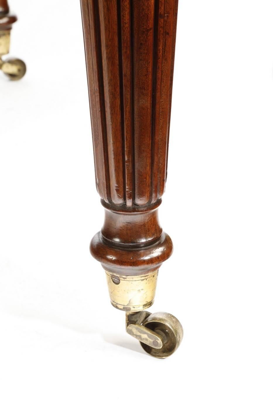 Table à écrire Regency en acajou bien figuré, de forme rectangulaire avec un plateau en cuir vert, un long tiroir et deux courts tiroirs dans chaque frise, reposant sur des pieds fuselés et cannelés avec les roulettes d'origine, vers 1810.