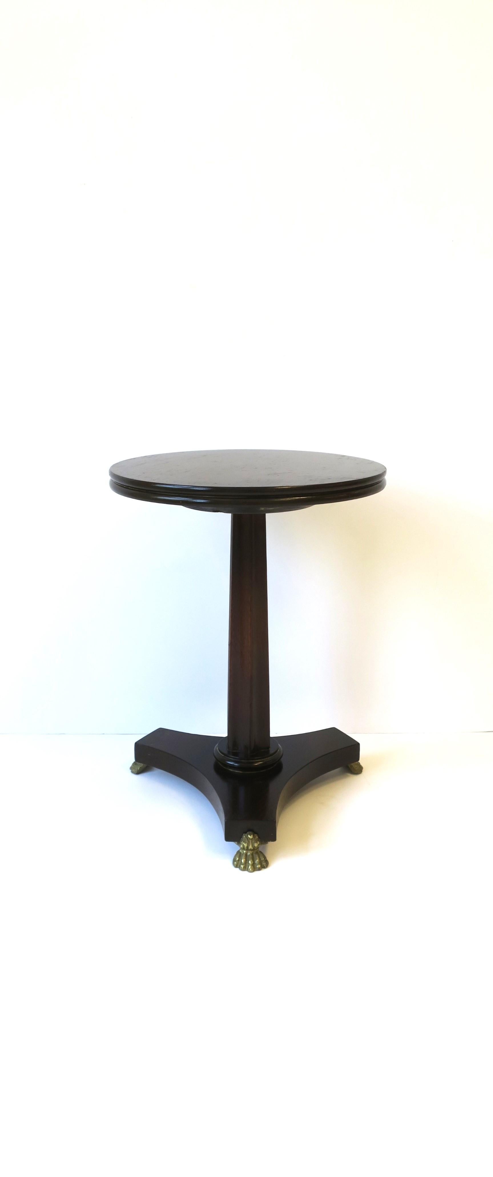 A rich dark brown wood side or drinks table with lion paw feet in the Regency style, circa mid to late-20th century, England. This side or drinks table has a round top and tri base with three brass lion paw feet. Table is a convenient size.