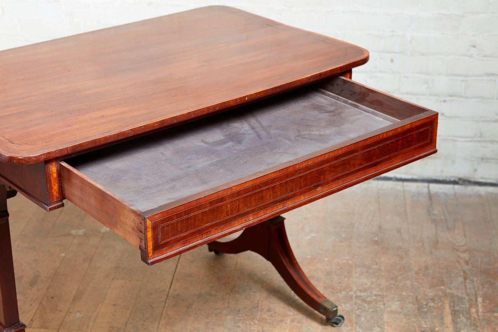 Good Georgian mahogany and satinwood cross banded writing table, the top having rounded corners with string inlay and satinwood banding, over single drawer similarly treated and standing on trestle legs with inlaid down swept legs ending in boxed