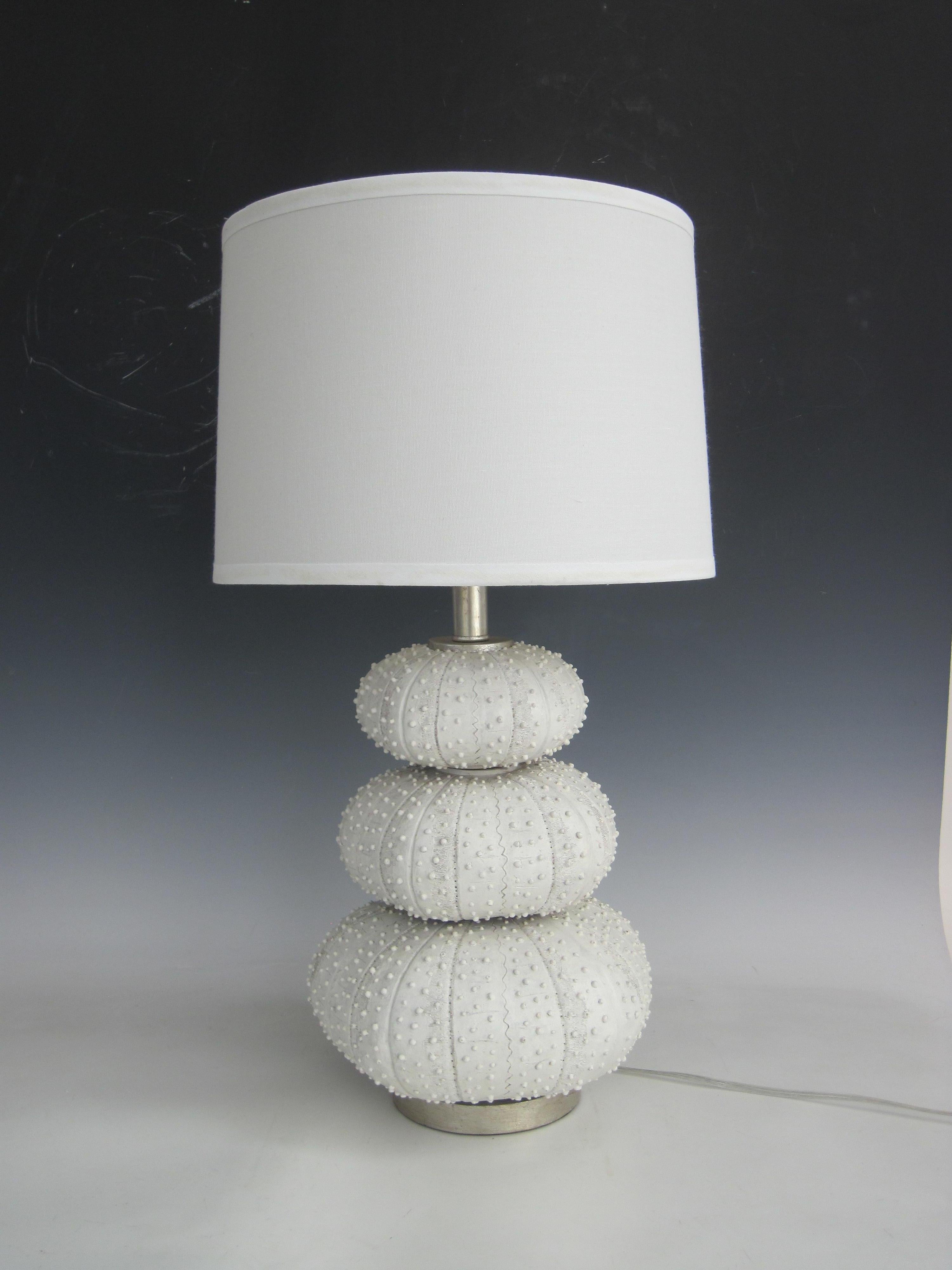 Lampe de table en faux oursin empilé de Regina Andrews (attribuée) avec quincaillerie en ton argenté brossé. Les oursins montés individuellement ont une finition naturelle colorée au sel de mer. Utilise une ampoule à 3 voies de 150 watts.
Abat-jour
