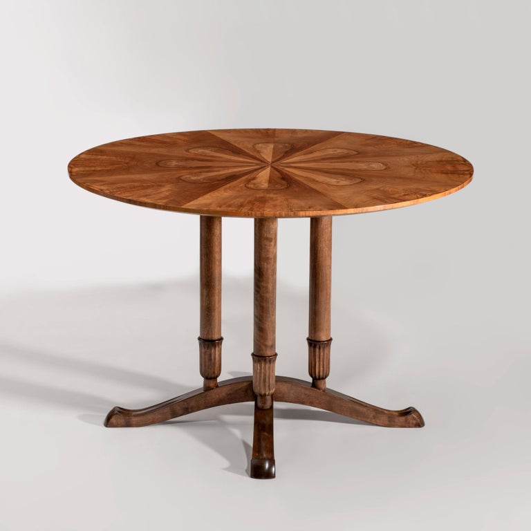 The circular top adorned in eight book-matched flame walnut panels, raised on four columnar birch legs, each issuing from a bellflower base, terminating in splayed s-form legs. Stamped: R and three crowns within a triangle (for Reiners Mobelfabrik);