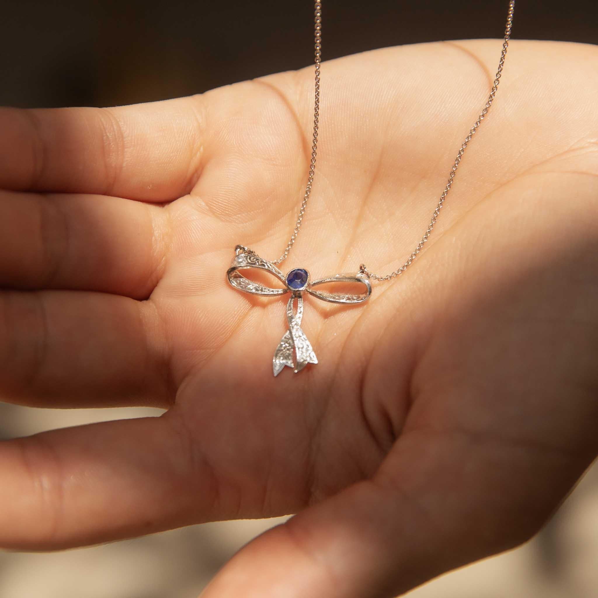 This exquisite necklet features a stunning blue sapphire wrapped in a ribboning bow of diamond-embellished 18 carat white gold. All vivid blue and shimmering light, she exudes a sense of grace and femininity. We have named her Sienna, the perfect