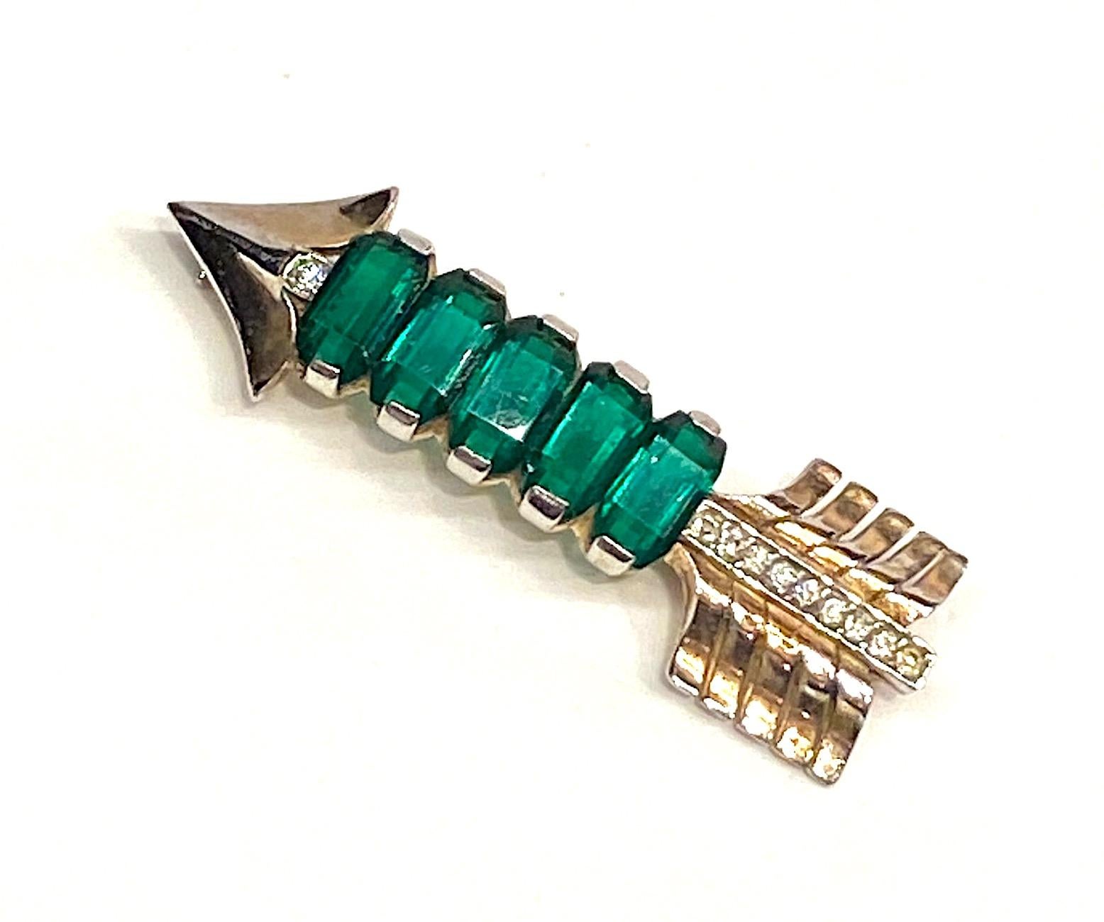 A lovely vintage sterling silver vermeil arrow pin brooch that was featured in Women's Wear Daily on February 24, 1943. This piece was designed by Solomon Finkelstein for Reja in 1943. It is set with five open back rectangular faceted emerald color