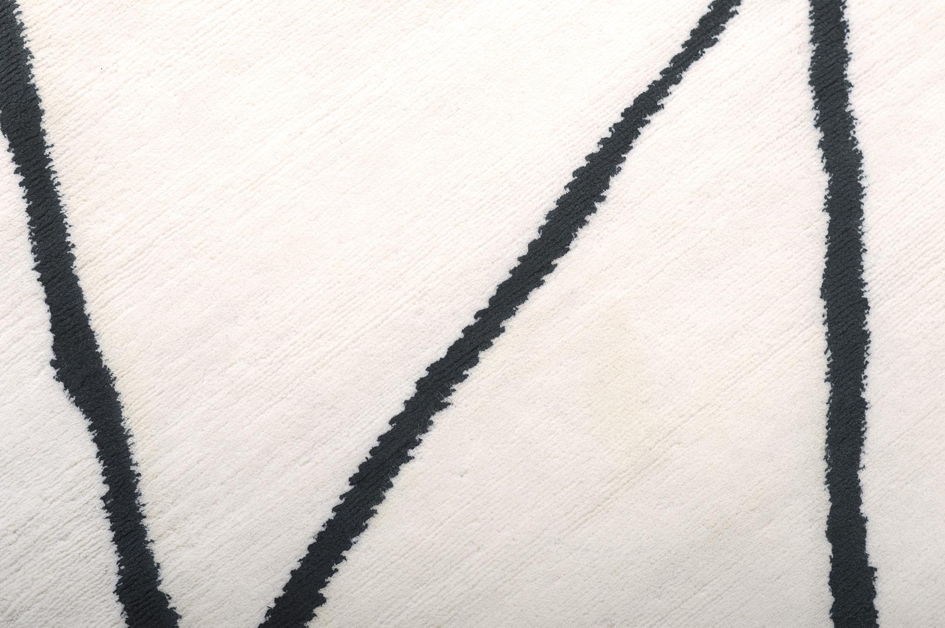 'Release' is a handwoven modern abstract rug made of wool and silk. It is a part of the Design Rhymes Collection which pulls inspiration from different aspects of architecture. The contrasting black lines creating cracks through the white rug makes