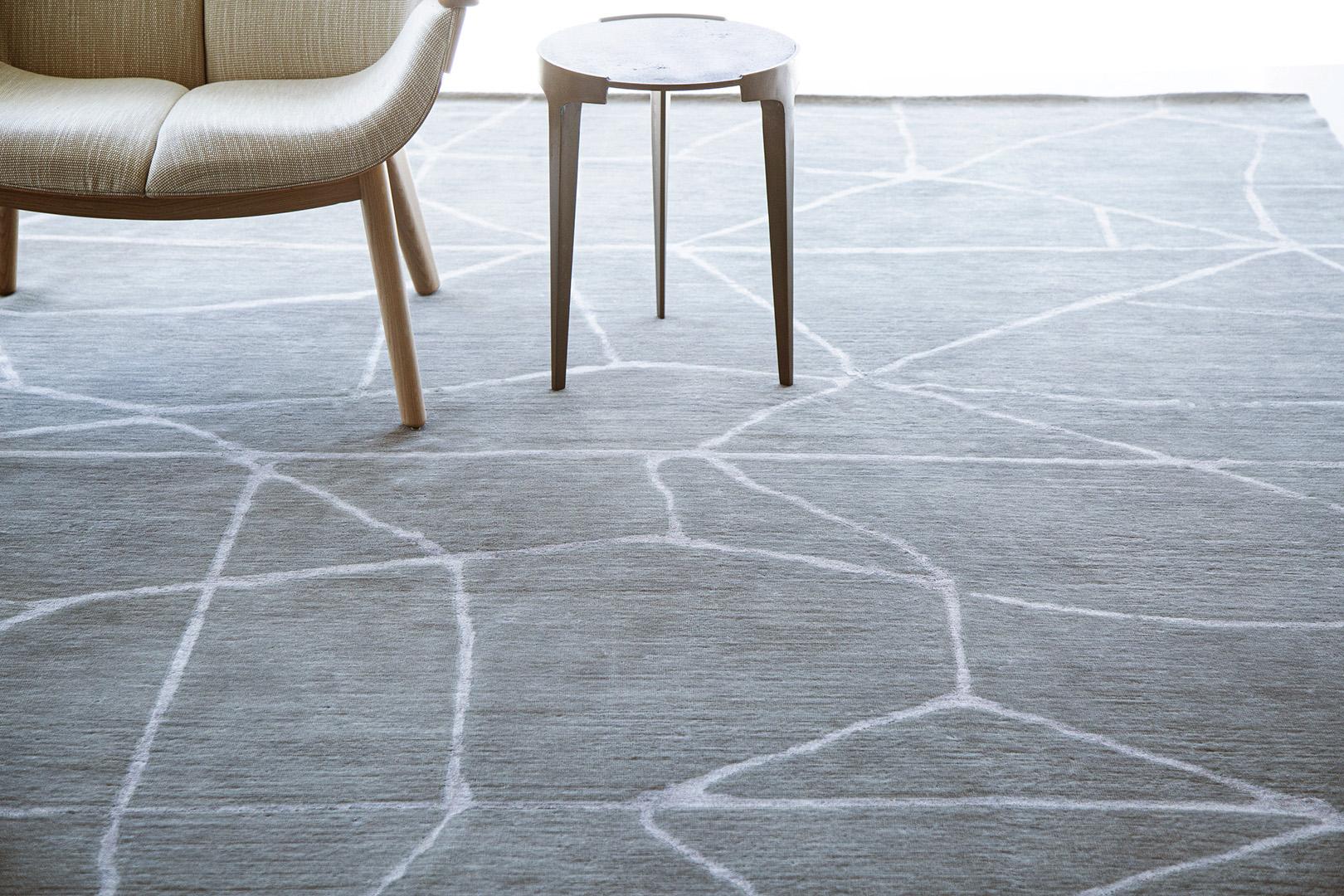 'Release' is a handwoven modern abstract rug made of wool and silk. It is a part of the Design Rhymes Collection which pulls inspiration from different aspects of architecture. The contrasting white lines creating cracks through the slate grey rug
