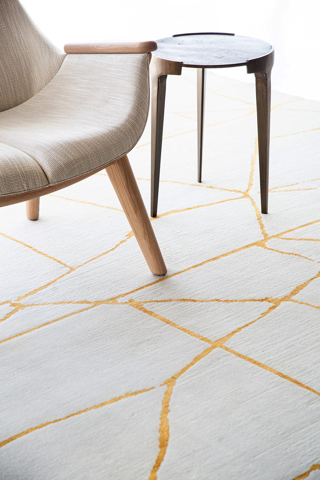 'Release' is a handwoven modern abstract rug made of wool and silk. It is a part of the Design Rhymes collection which pulls inspiration from aspects of architecture. Strong contrasting gold lines create cracks through the white rug making a