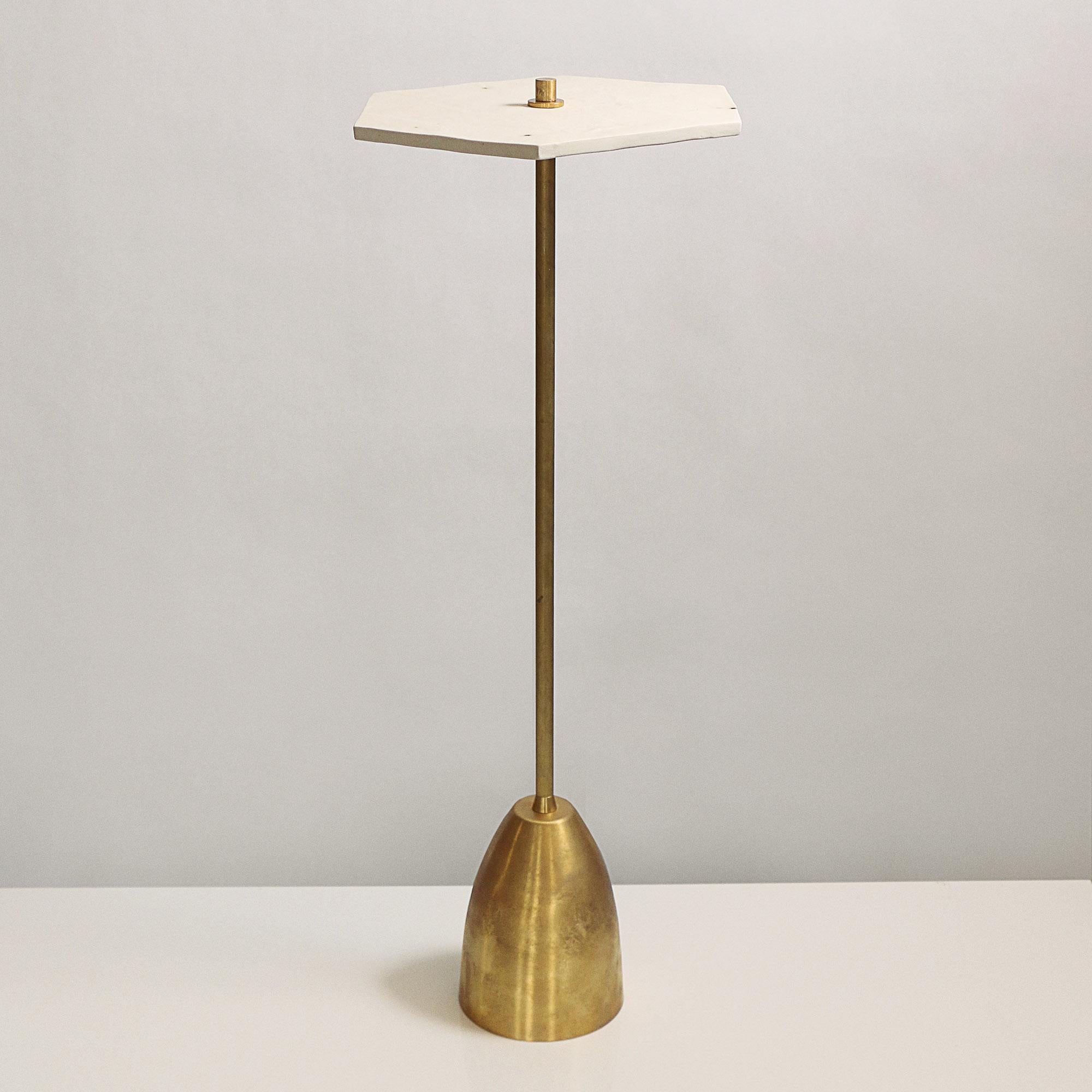 This elegant drinks table features a hexagonal top made from handcrafted satin unglazed white porcelain. Each top is individually handmade, so no two are exactly alike. The porcelain tabletop balances on a slender unfinished brass rod and a weighted