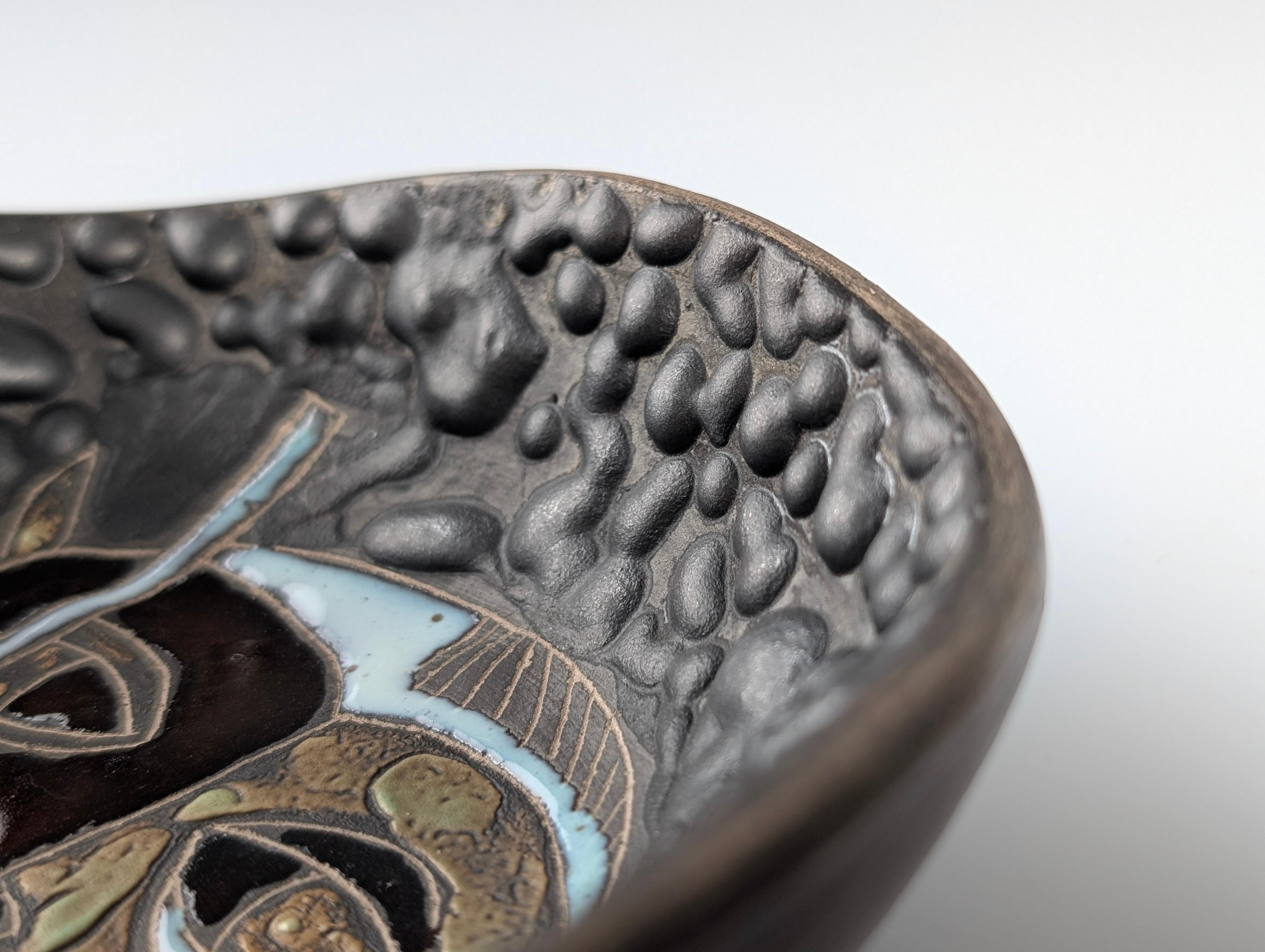 This mid-century modern ceramic bowl, attributed to Marcello Fantoni from the 1950s, represents a work of unique and expressive design. Its relief surface combines organic textures with an abstract composition, featuring a central motif that evokes