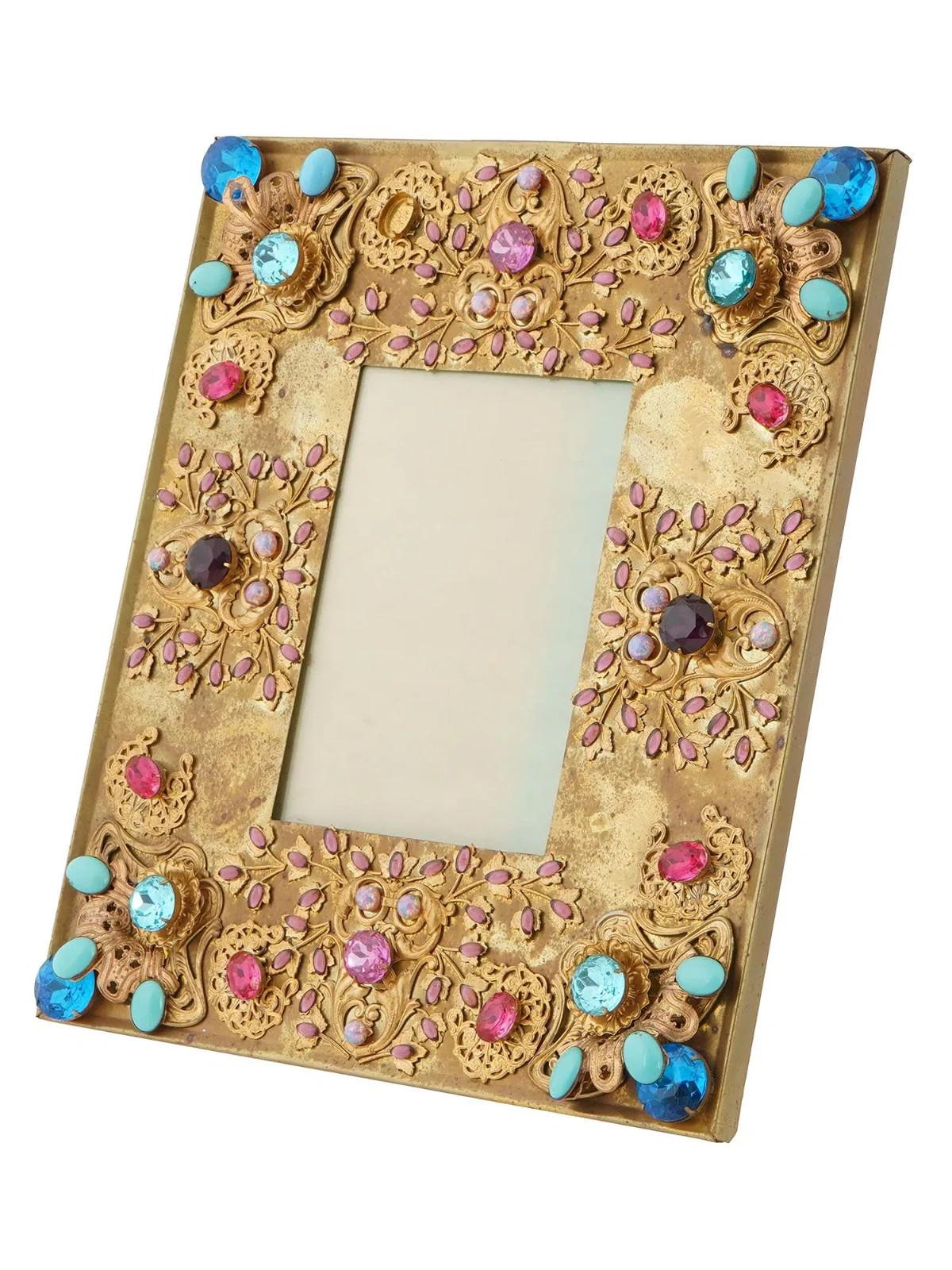Vintage-Bilderrahmen aus vergoldetem Messing. Der Rahmen weist ein Reliefdesign auf, das mit dekorativen Elementen wie bunten Steinen und Perlen vor einem goldfarbenen Hintergrund verziert ist. Das Geschirr ist mit reliefierten Blumen-, Laub- und