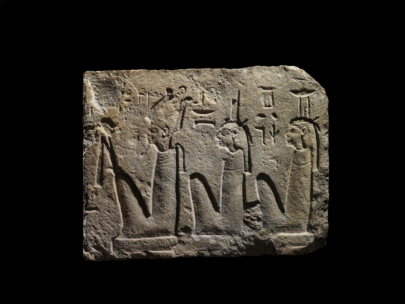 A fragment of indurated limestone carved in sunk relief. A row of three shrouded deities are depicted seated, facing left, each wearing a broad collar and characteristic crown. Osiris is shown with pharaonic beard and his typical feathered atef