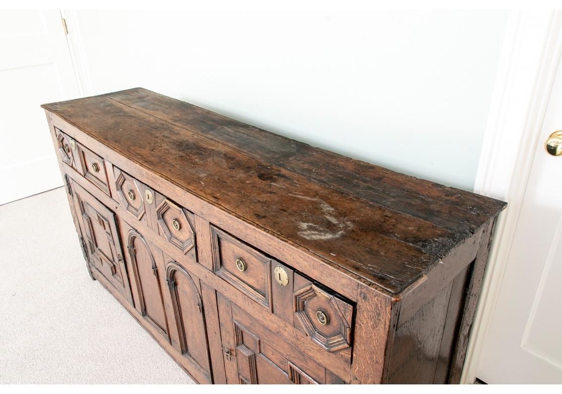 A Time-Worn Antique Continental Server Cabinet in Oak. The three apron drawers with deep carved moldings in rectangular and octagonal shapes, and brass ring pulls. Lacking a key. Two side doors with deep carved angular moldings, iron hinges and