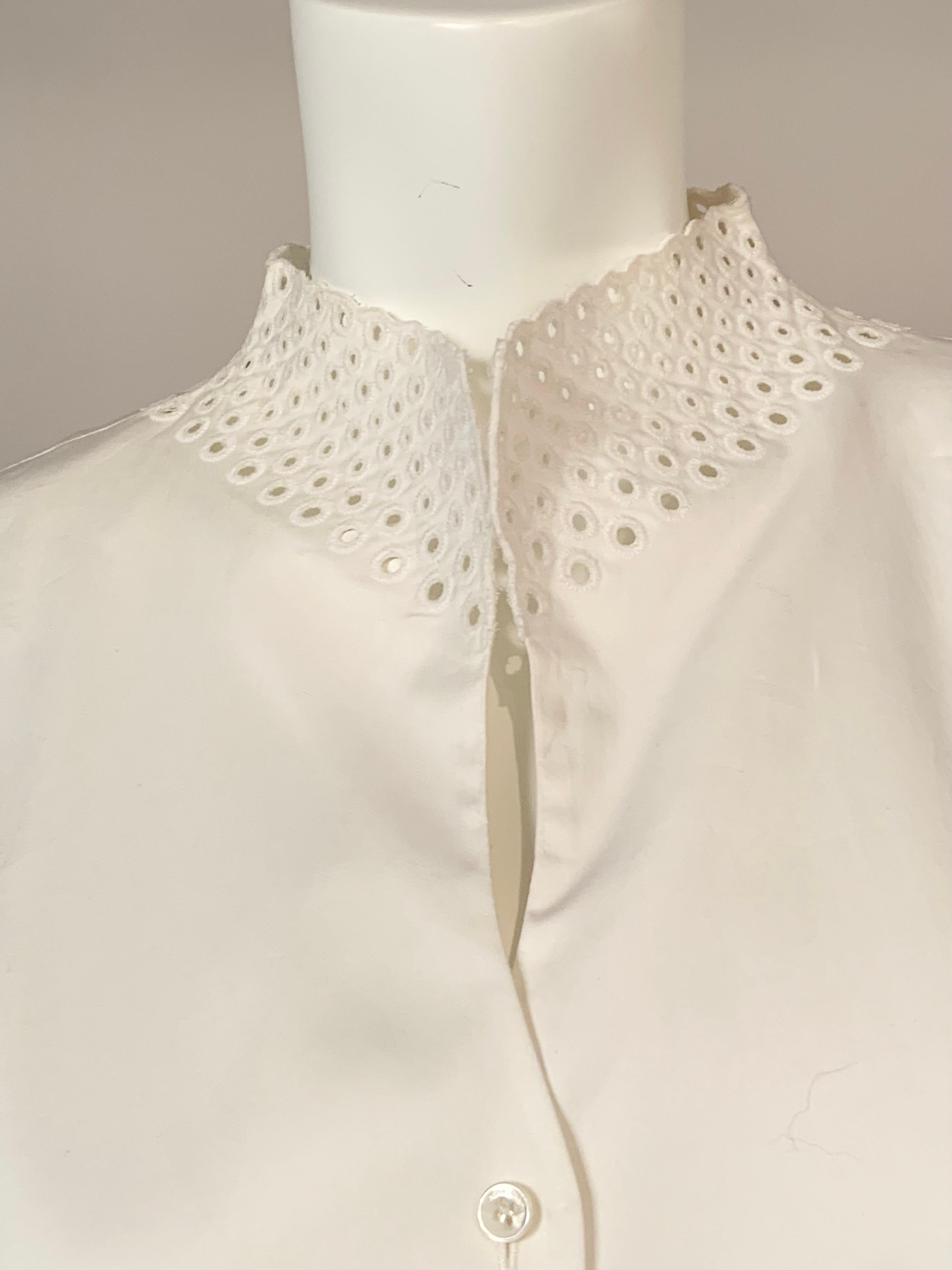 This feminine white cotton blouse from Rena Lange has cut work and embroidered details on the stand up collar and the sleeves.  The blouse has five buttons at the center front.  It bears the original hang tags and extra button and is in excellent