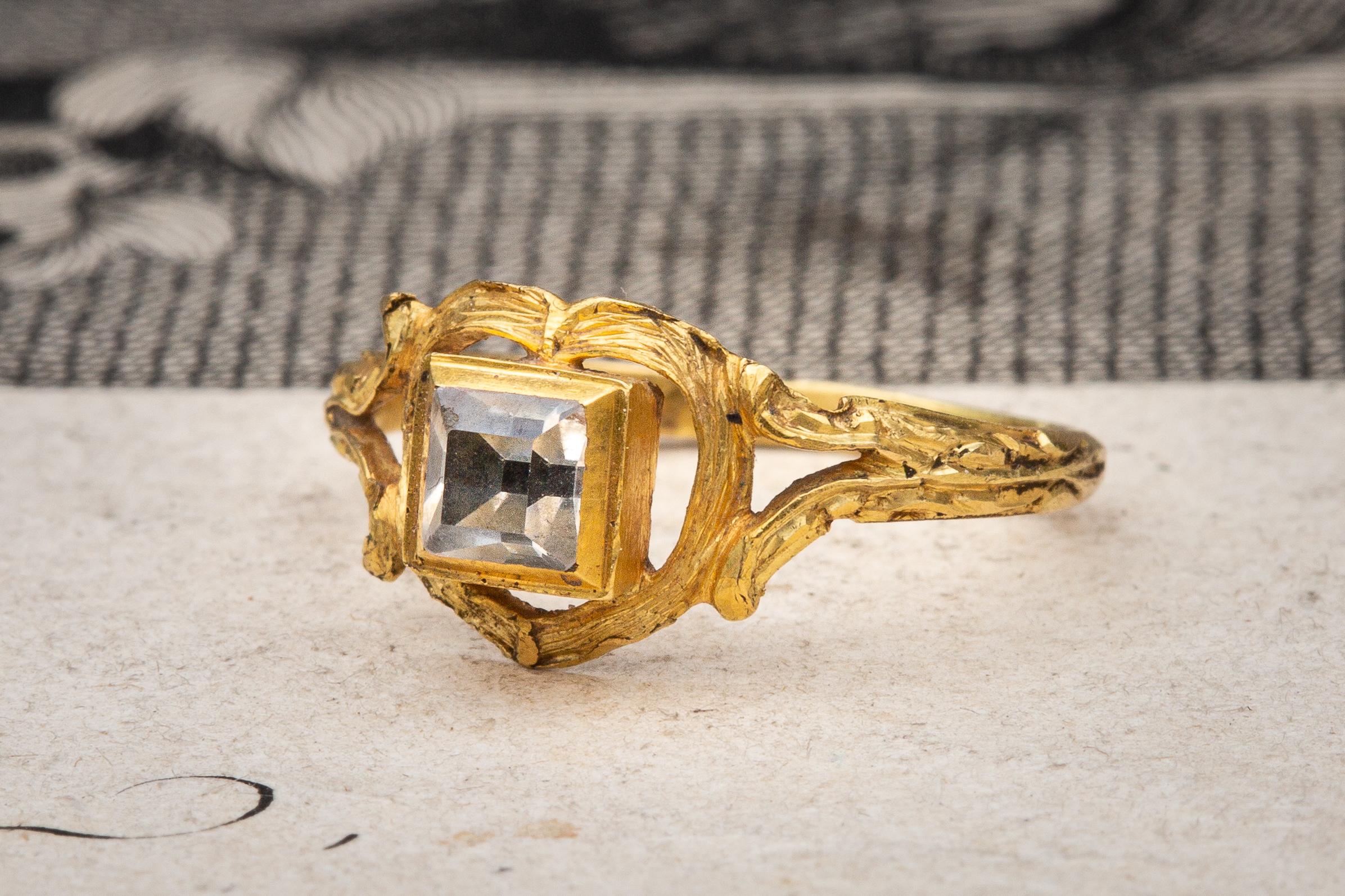 A stunning example of a Western European renaissance ring dating to around 1650! A high table-cut rock crystal is mounted in a closed back rub over box setting. The square bezel with its bevelled edges is bordered by an openwork heart motif with