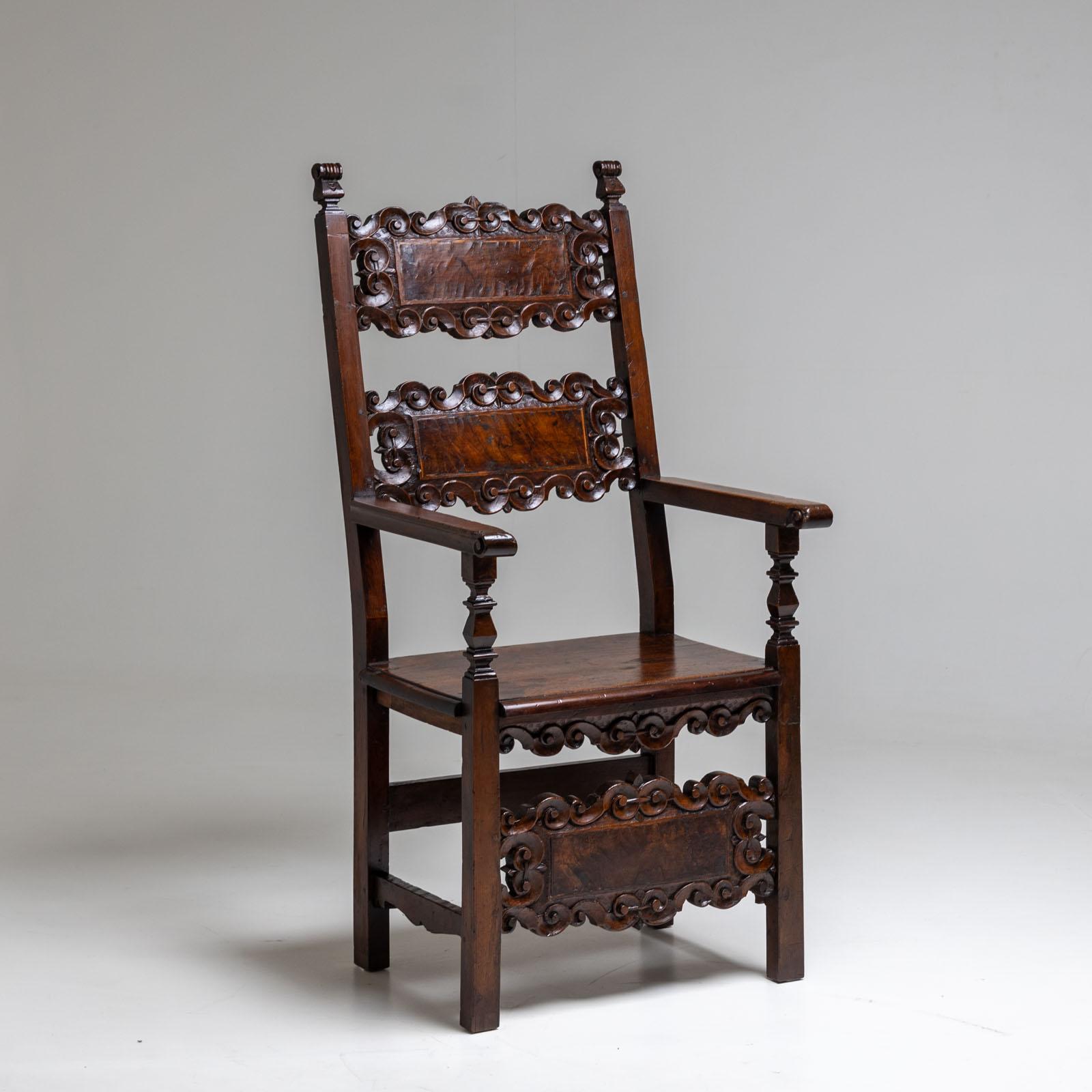 Armchair made of solid walnut with carved pinnacles and volute-decorated intermediate struts on the backrest and front legs. The straight armrests rest on baluster-shaped supports. Beautiful authentic patina.