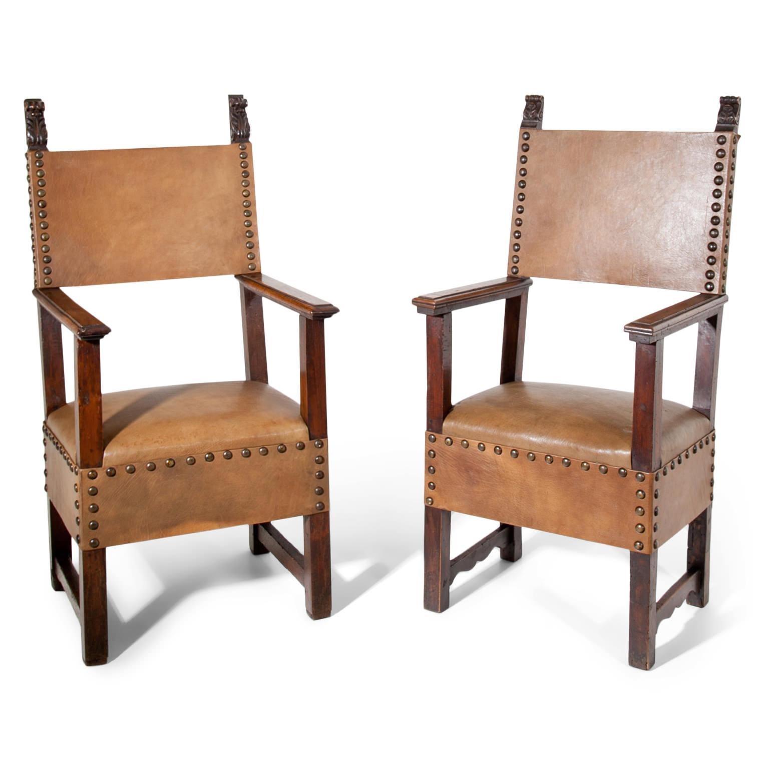 Renaissance armchair out of walnut, seat and backrest are covered with a brown leather and riveted. The chair stands on straight square legs that are connected on each side. The straight armrests slightly protrude over the elongated front legs. Very