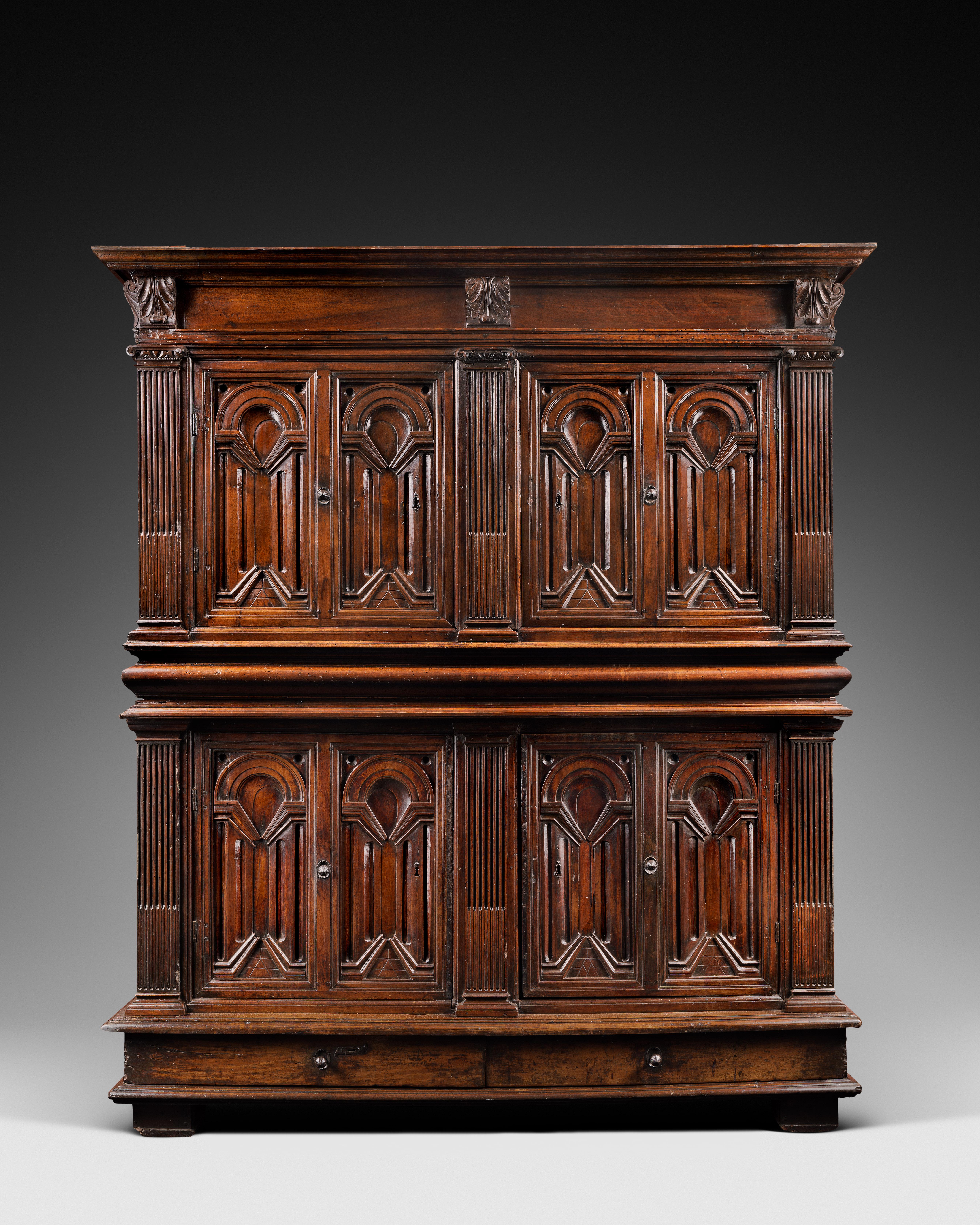 A rare carved walnut wardrobe opening with four door-leaves and two drawers in the lower part. The doors bear architectural views in low reliefs, fluted pilasters and Ionic capitals.

Upper Body
Two door-leaves with carved architectural
