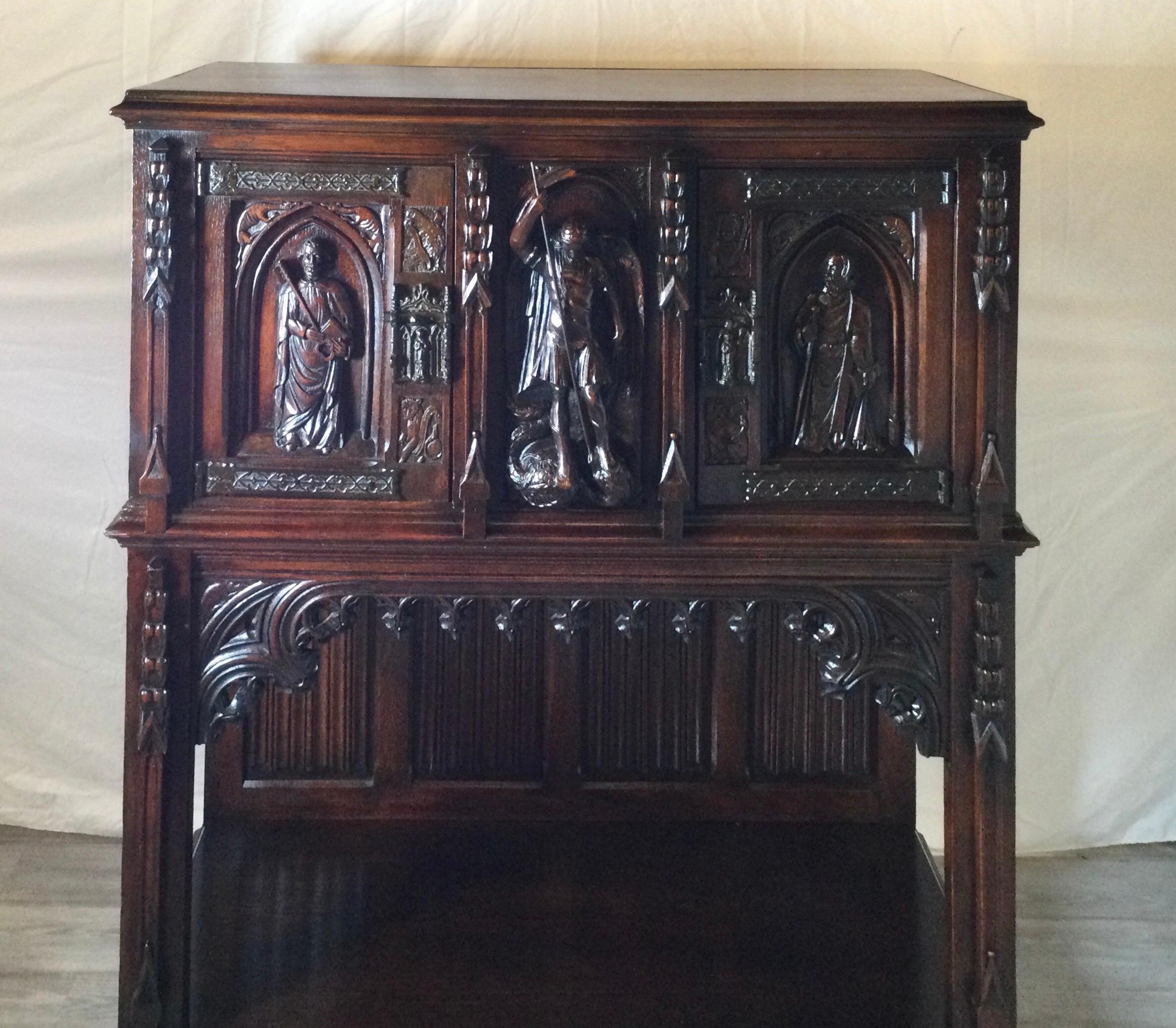 Hand carved dark oak court cupboard with three saints across the front panels. The center being Saint Michael. The two doors at the top with a center stationary panel, above the open display, storage area, Belgium, Circa 1890's.