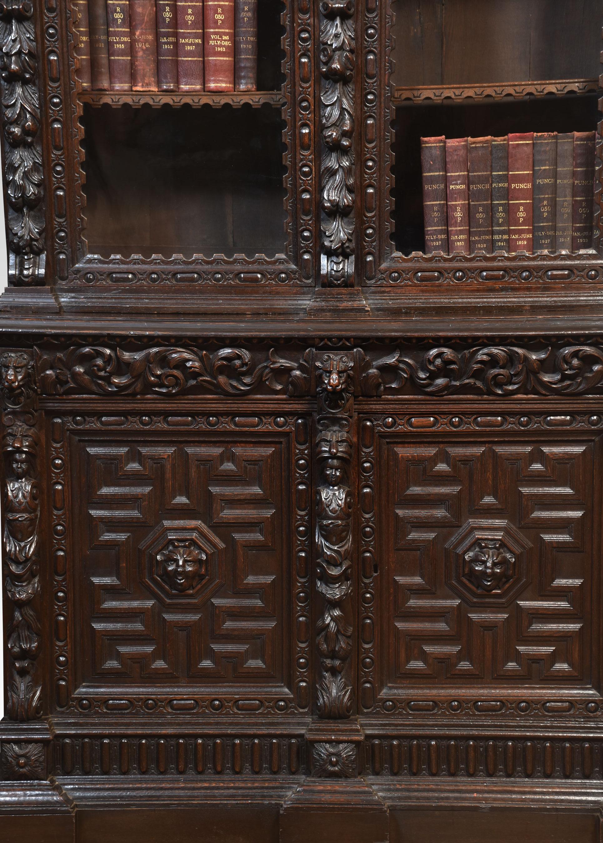 Renaissance revival carved oak two-door bookcase, the deep cornice above two large glazed doors enclosing shelved interior, flanked by pilasters carved with scrolls and figural masks. To the base section with a long drawer over two carved cupboard