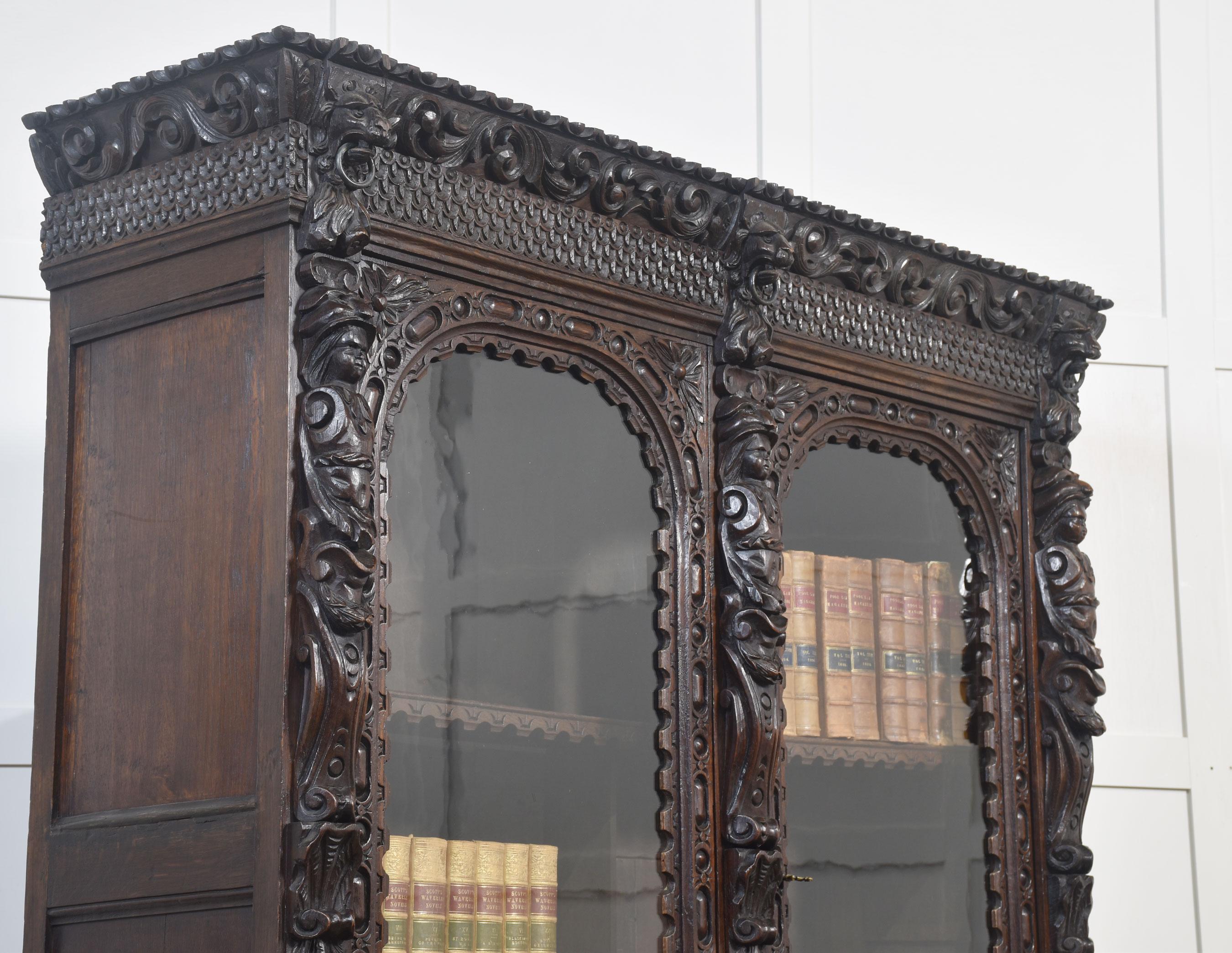 Libreria a due ante in legno di quercia intagliato in stile rinascimentale, con un profondo cornicione che sovrasta due grandi porte vetrate che racchiudono l'interno a ripiani, fiancheggiate da pilastri intagliati con volute e maschere figurative.