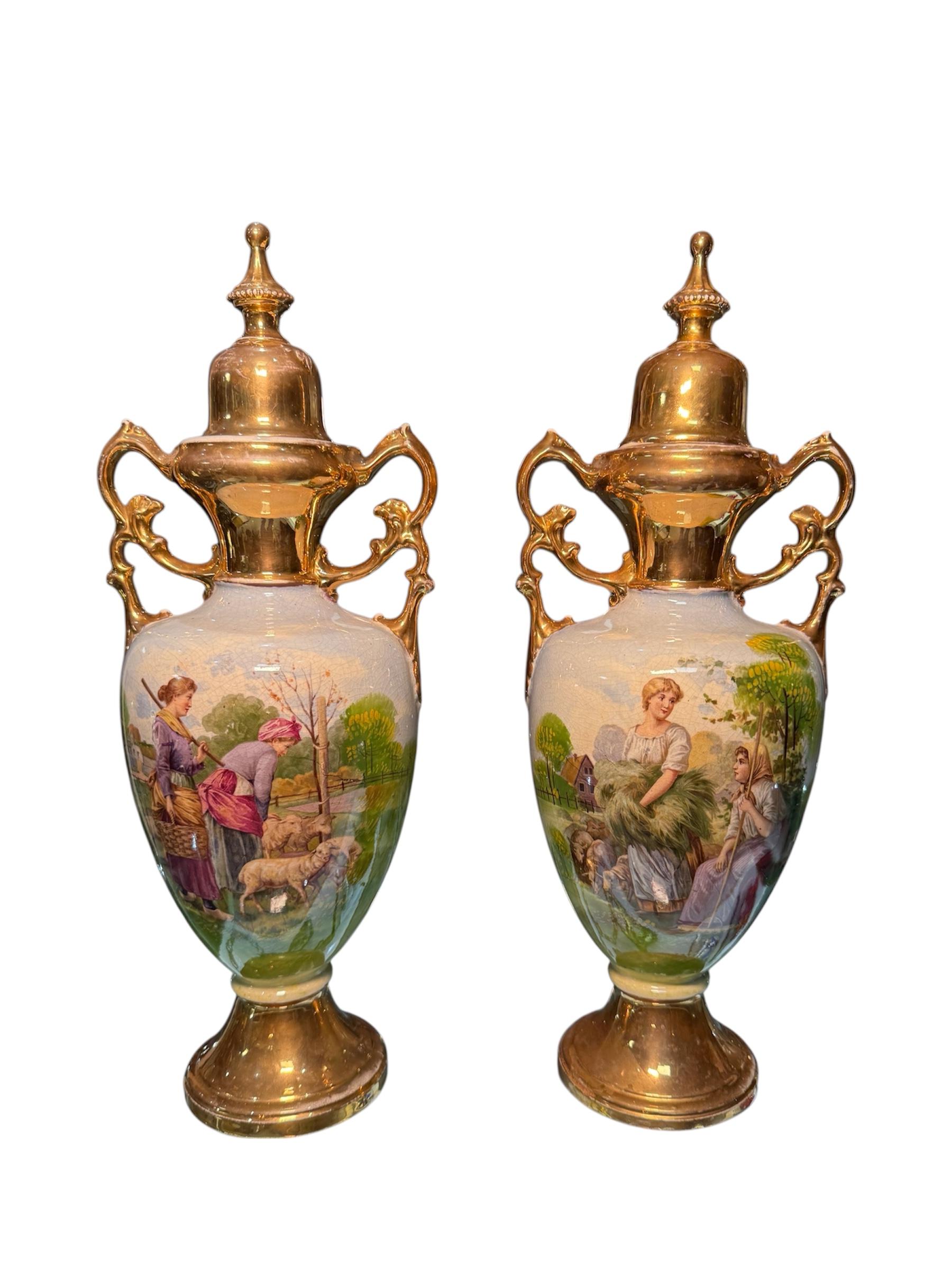 Questa è una coppia di A.G. Urne in porcellana di Harley Jones. Raffigura due urne di porcellana dipinte a mano con scene pastorali al centro del corpo e colori dorati sui manici, sui coperchi, sui colli e sulla base. Coppia di rami dorati a forma