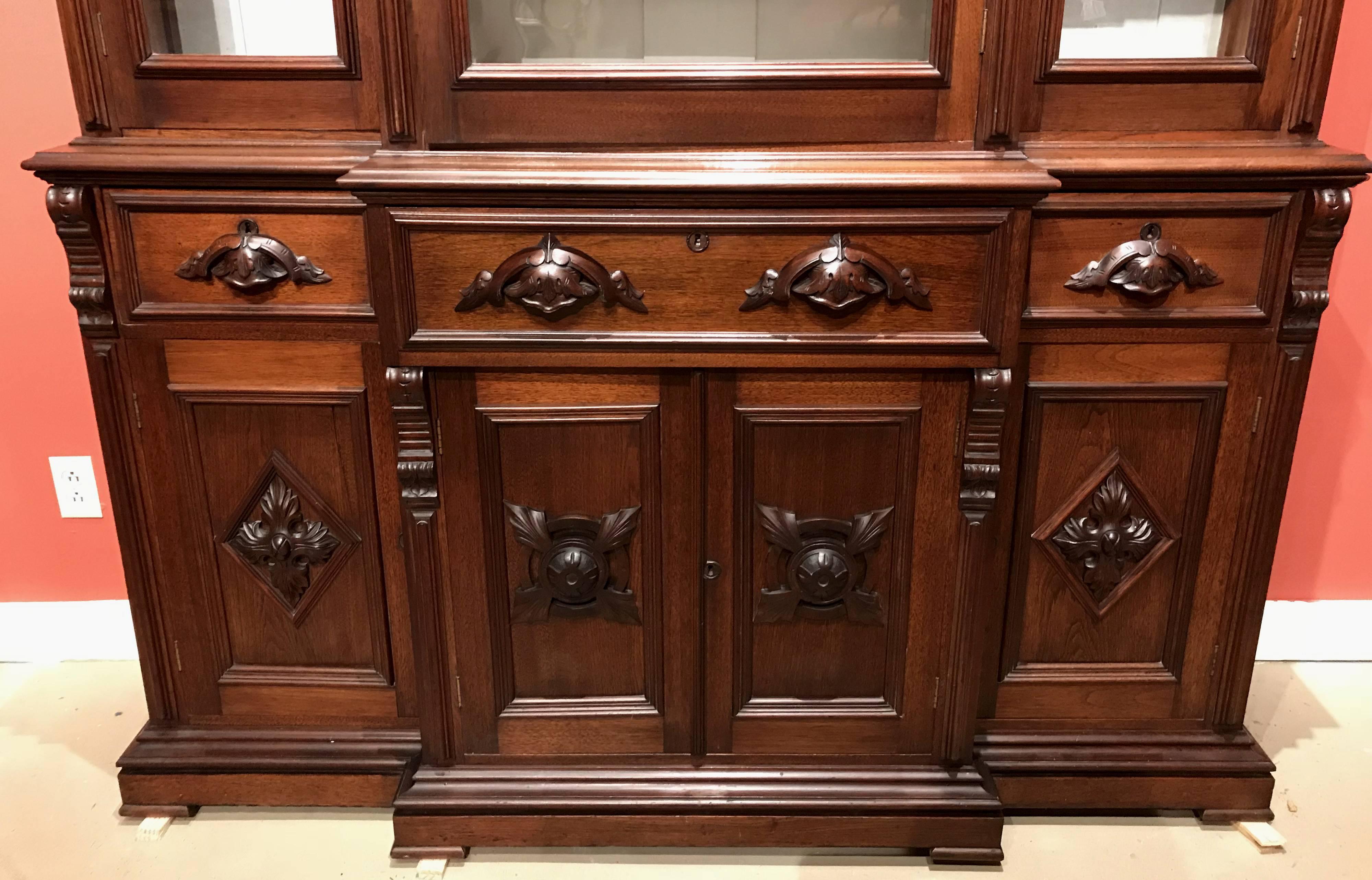 A fine Renaissance Revival Victorian two part walnut cabinet, its upper bookcase section with three glazed glass doors with molded surrounds and centre carved crest decorations, which open to a painted white interior with three adjustable