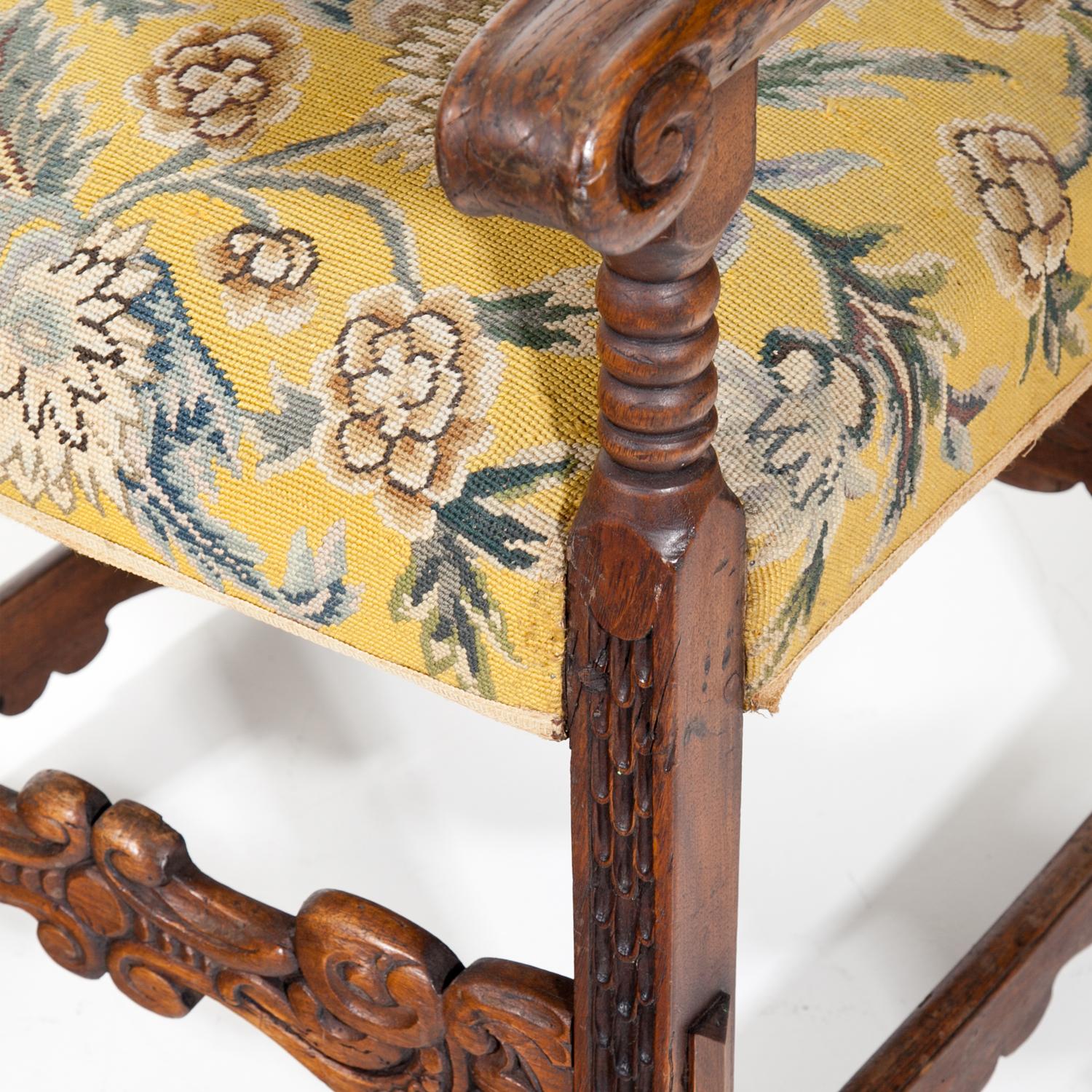 Renaissance style armchair standing on a walnut base with scales- and leaf-décor. The armchairs slightly descend towards the legs and end in volutes. Seat and backrest are covered in a yellow fabric with flower décor.