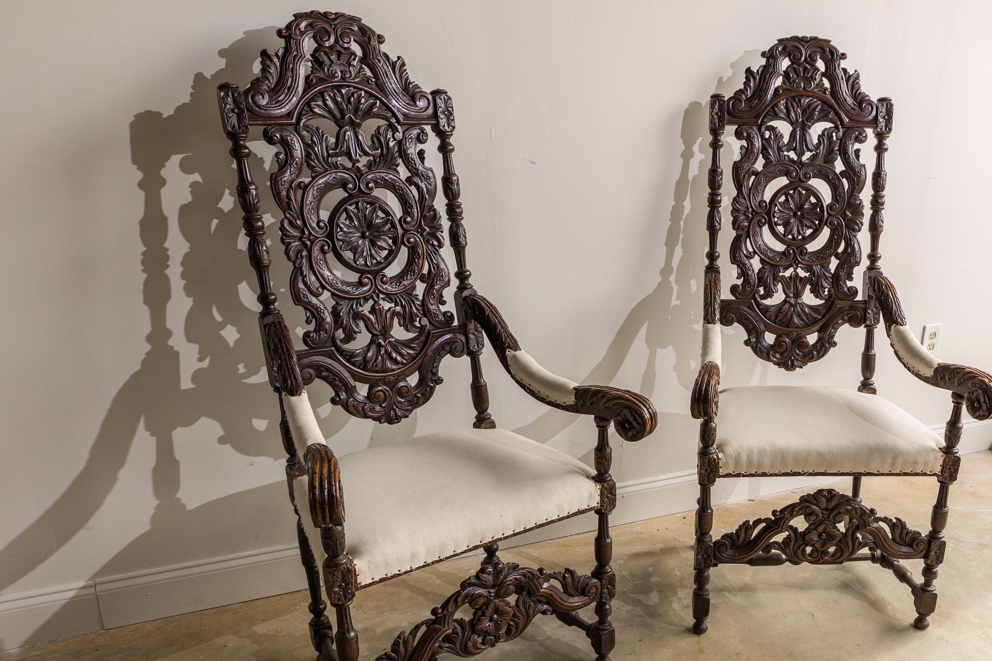 This pair of Renaissance style Italian armchairs look to be fit for a king. The tall seat back has beautiful hand carved wood and aged dark painted finish. The wood species is unknown. It is upholstered in a simple white cotton fabric with small