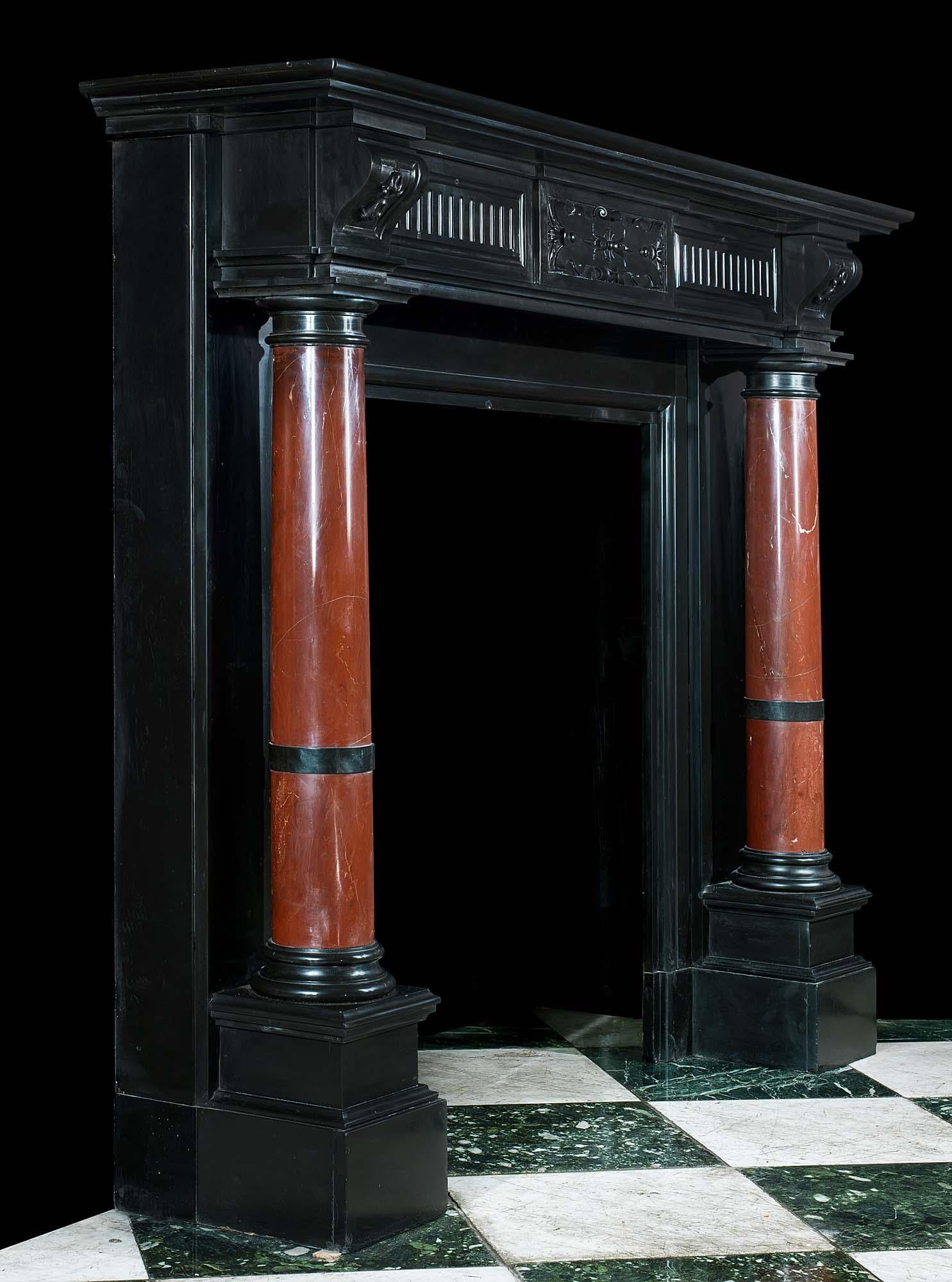 An elegant high Renaissance style polished Belgian black marble antique fireplace mantel. The fluted panelled frieze is centred by a strapwork tablet flanked by foliate detailed endblocks resting above Rosso Antico marble tapering, freestanding