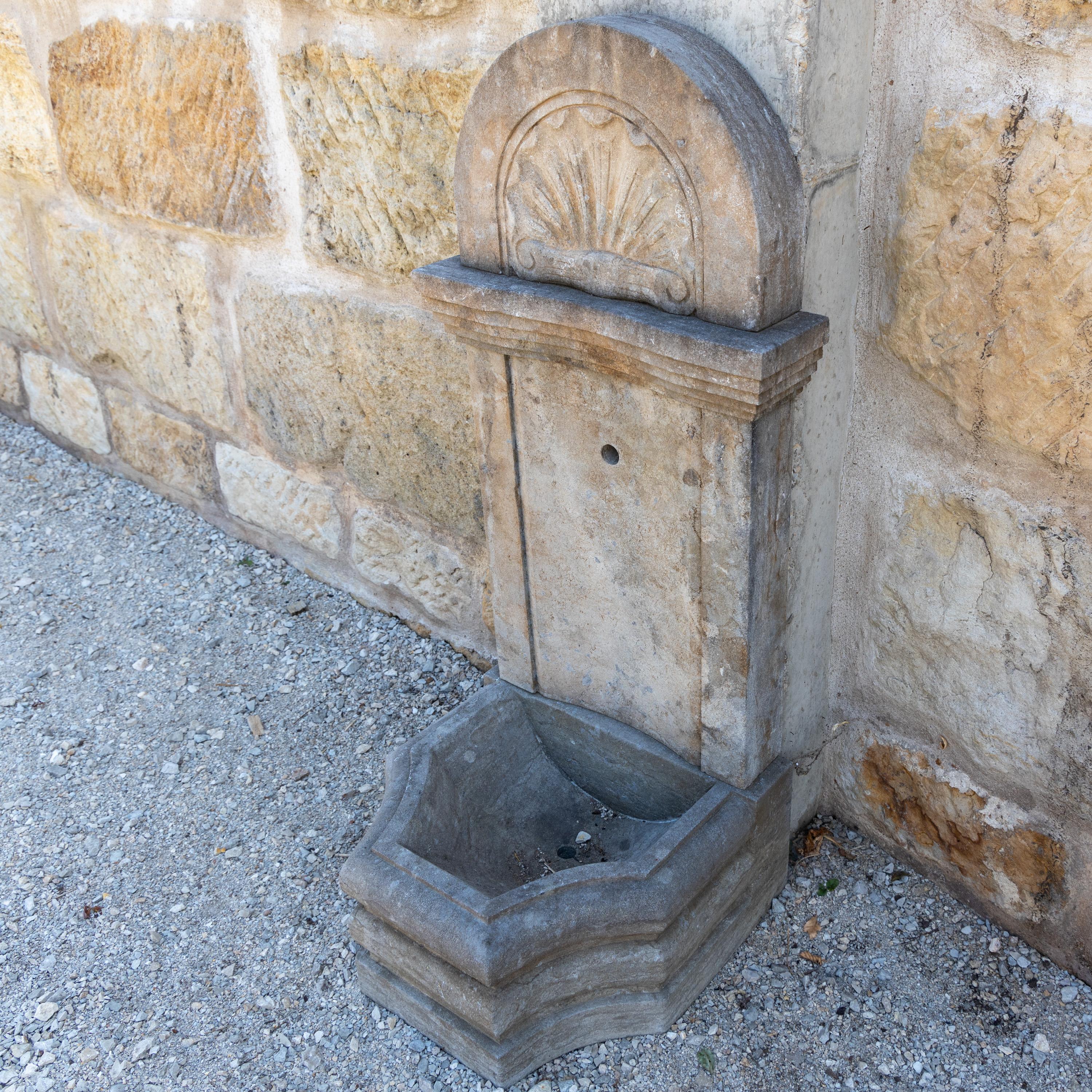 Wandbrunnen mit kleinem Becken mit profilierter Wand und segmentförmigem Aufsatz mit Muscheldekor.