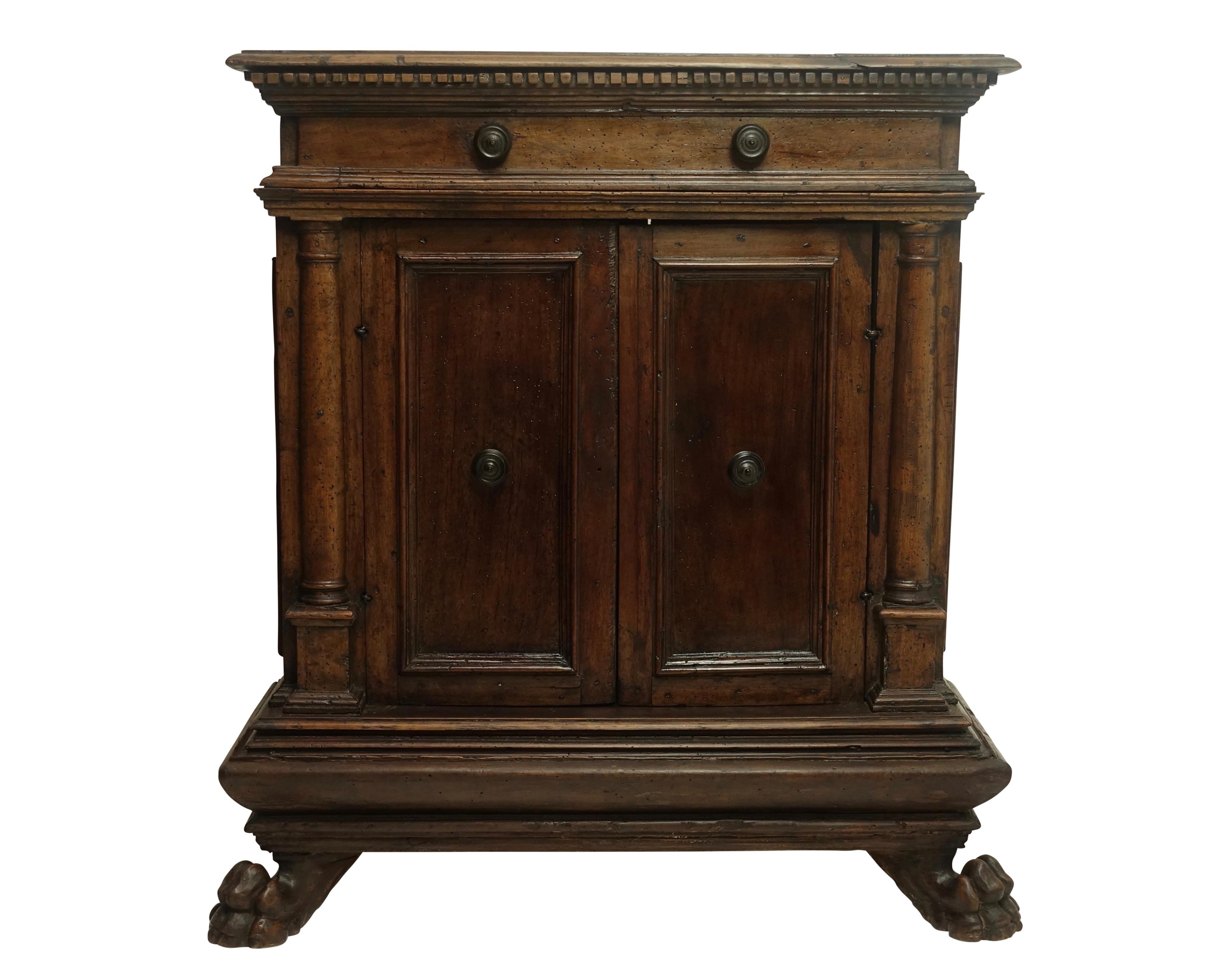 A tall walnut cabinet buffet, having a plank top with dentil moulding above a single drawer. The recessed paneled doors with iron pulls, flanked by Doric columns sitting on multi-moiled base, supported with wonderfully carved lion paw feet on the