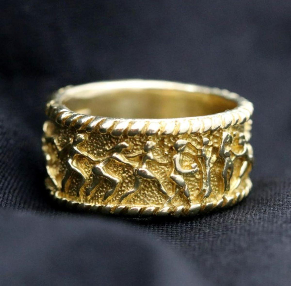 An 18 karat yellow gold band with a mill grained edge, depicting a scene of Adam and Eve in the garden of Eden. The texture and relief add depth to this handsome ring. Designed by Renato Cipullo, it measures 7/16 inches wide, and is a size 11 3/4.