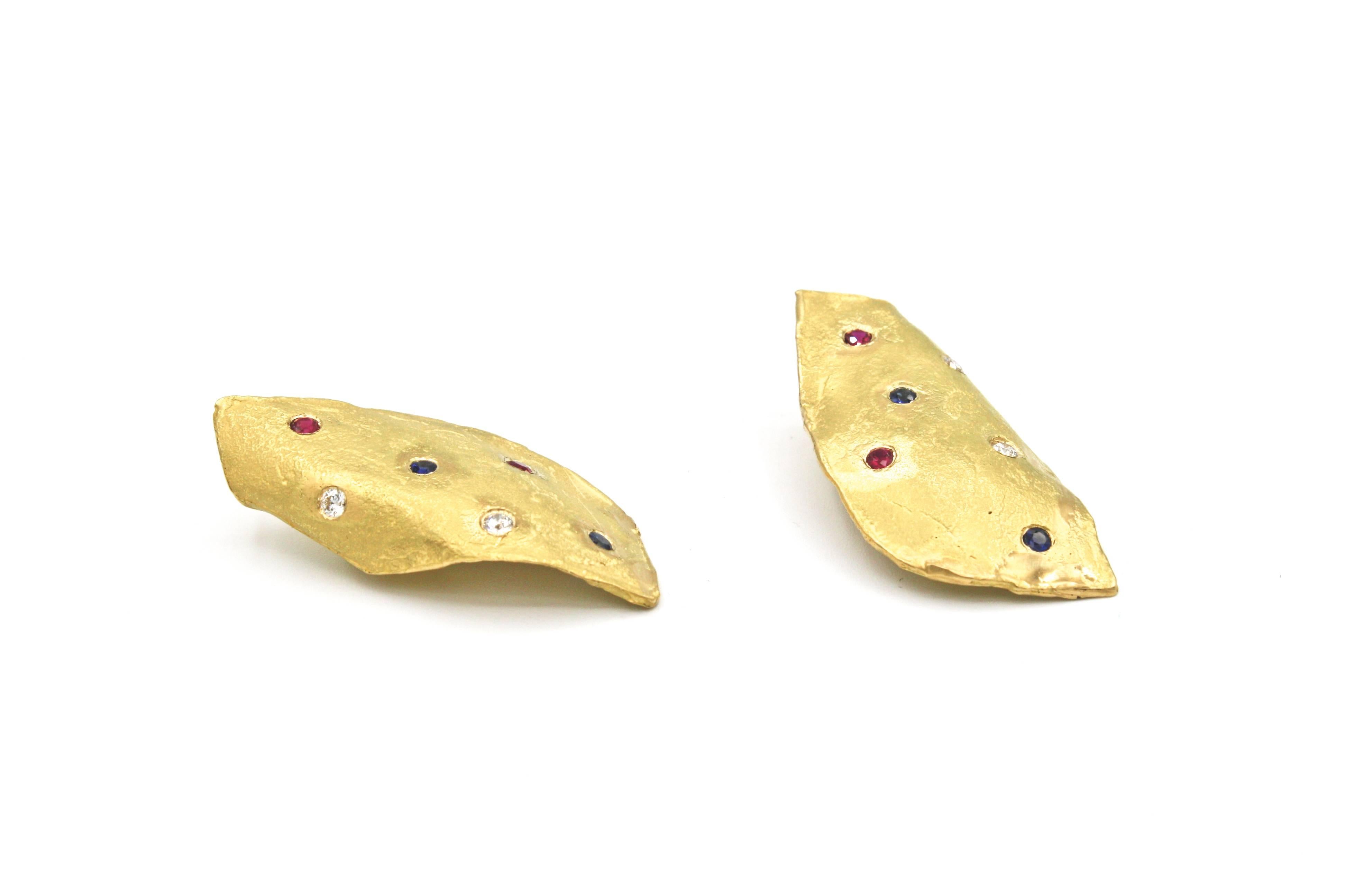 Inspired by the beach and the sea these 18k yellow gold earrings feature diamonds, rubys, and sapphires as well as a gold clip.  The rustic finish is designed by Renato Cipullo to look as if they are an object of the ocean.