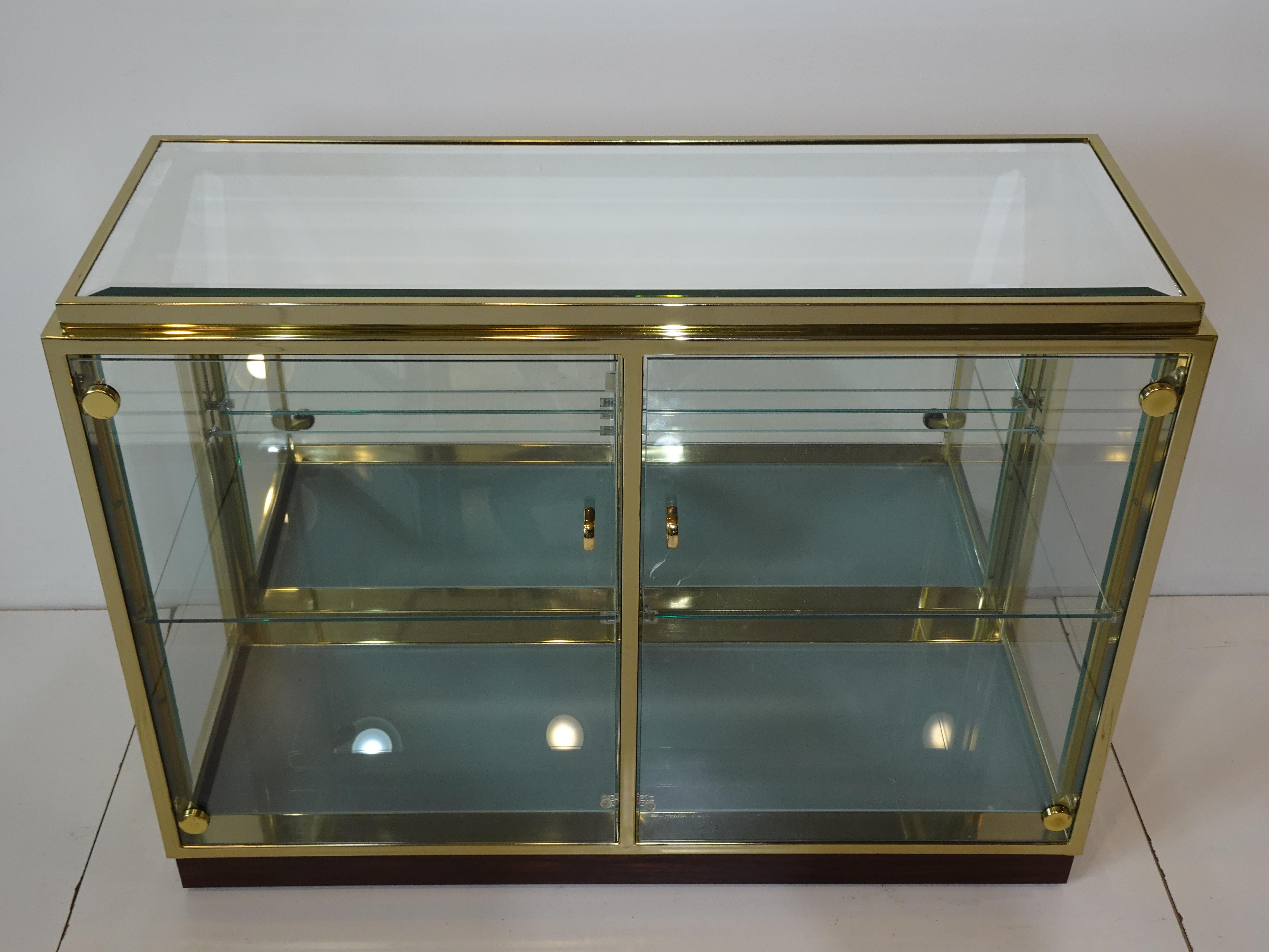 A very well crafted brass framed and rosewood bar cabinet with double glass doors and sides with beveled mirrored top and brass pulls . Inside the bottom has frosted glass with under lighting and two adjustable glass shelves to the inside for
