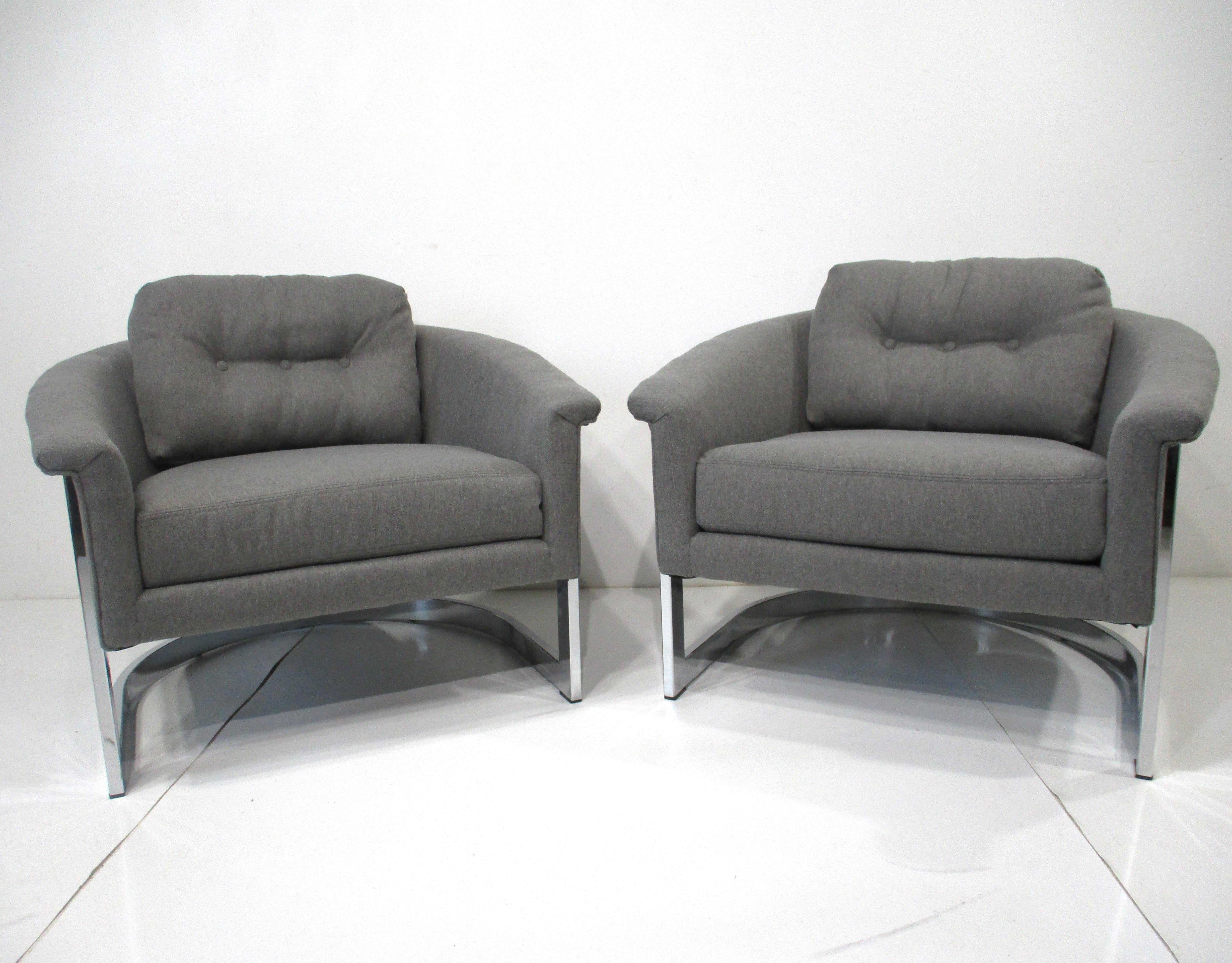 Une paire de chaises de salon très bien fabriquées avec des cadres sculpturaux en acier chromé et recouvertes d'un tissu contractuel doux gris moyen. Grâce à l'oreiller lâche du dossier et aux accoudoirs inclinés, ces chaises sont parfaites pour de