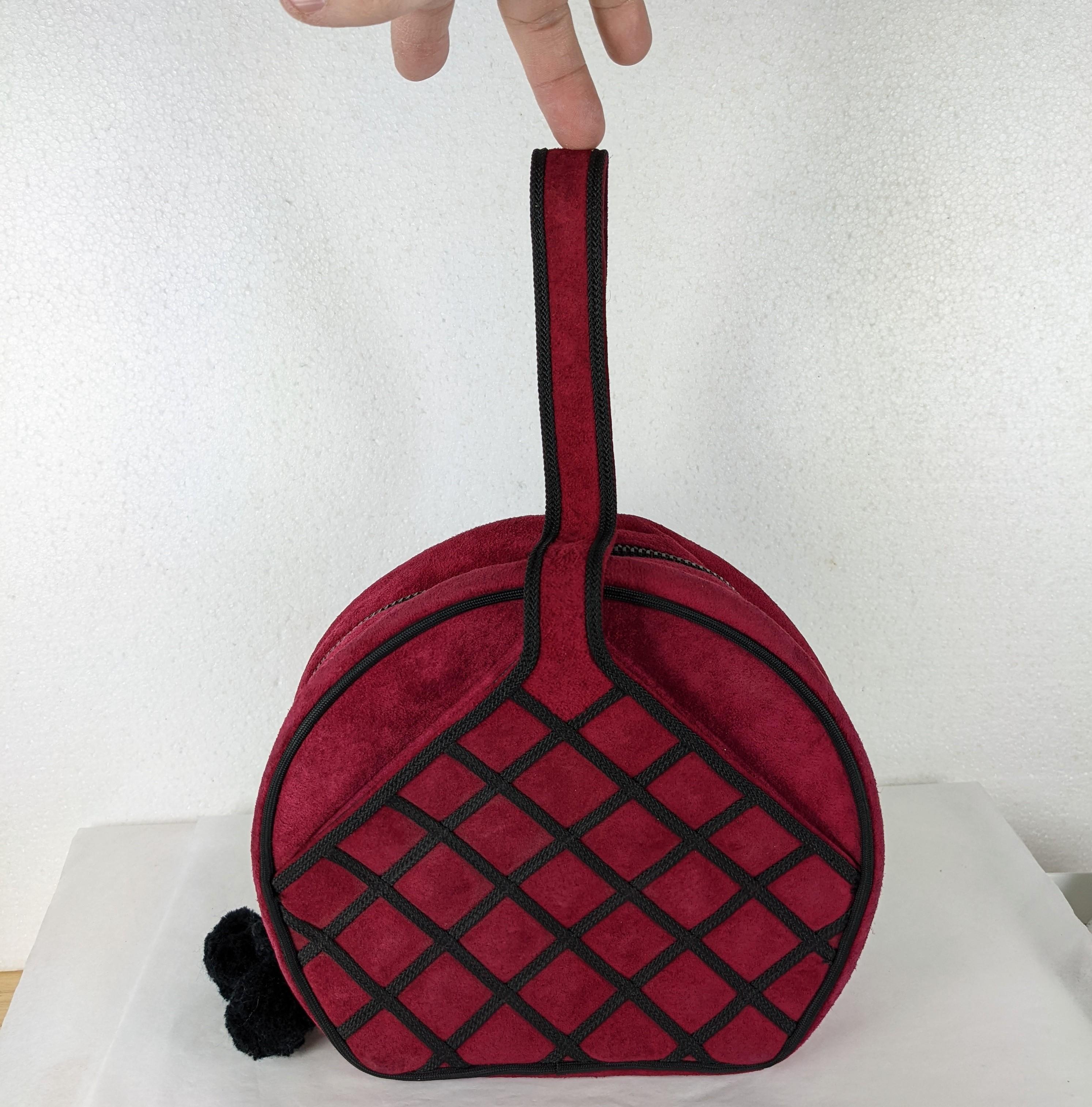 Renaud Pelligrino Deep Rasberry Suede and Soutache Bag from France 1990's. Unusual handled round bag with zip closure. Black soutache is stitched in a lattice work pattern and there are 2 side exterior pockets. Lined in black faille. Pom pom zipper